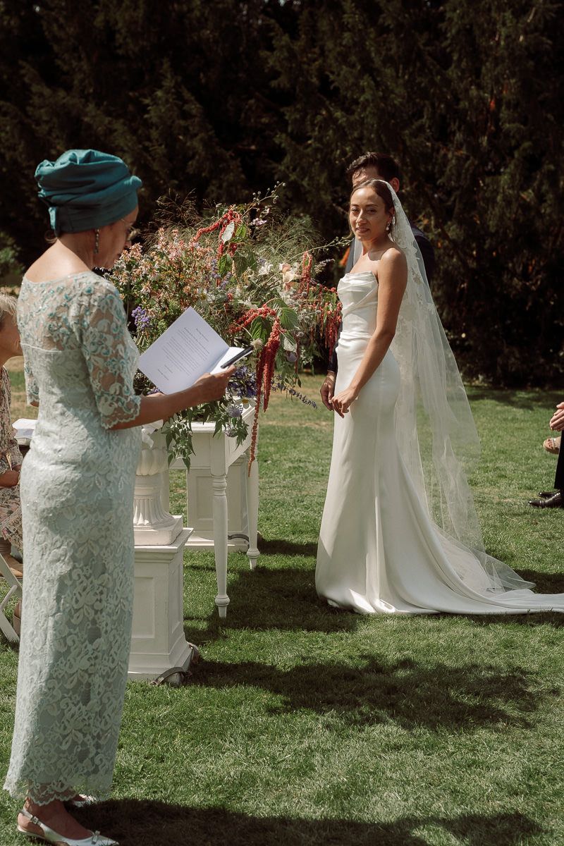 Two people share an emotional moment during an outdoor garden wedding ceremony with white columns and greenery.