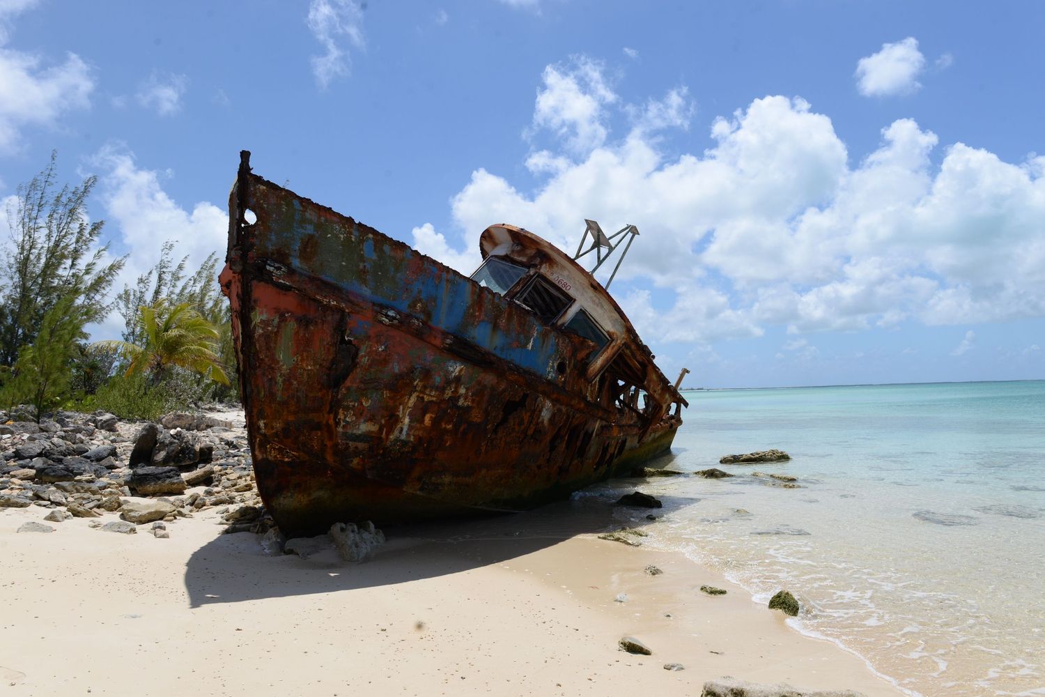 A rusted shipwreck on a tropical beach with turquoise waters and blue skies in the background.
