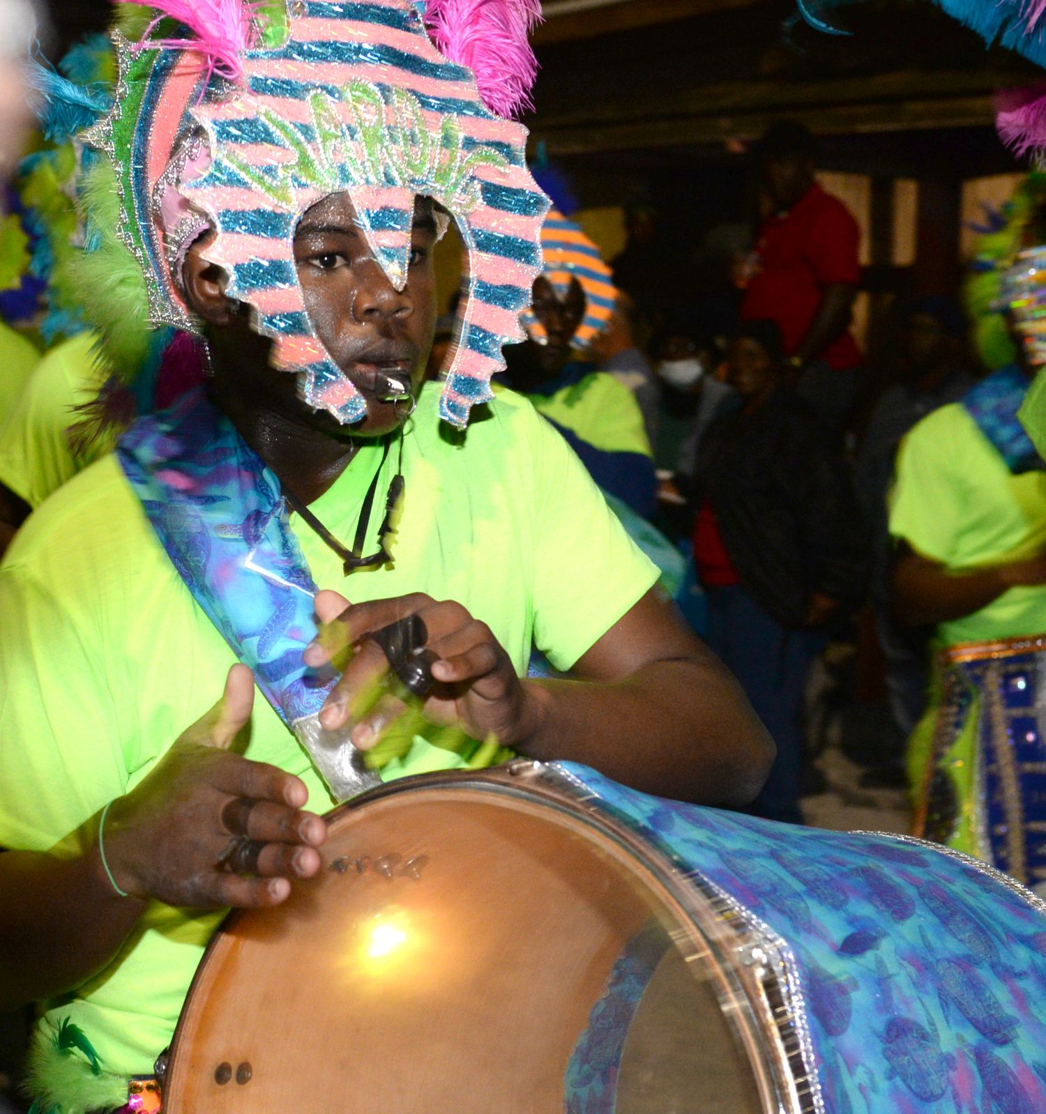 Carnival performer in neon yellow playing drums during a lively festival celebration.