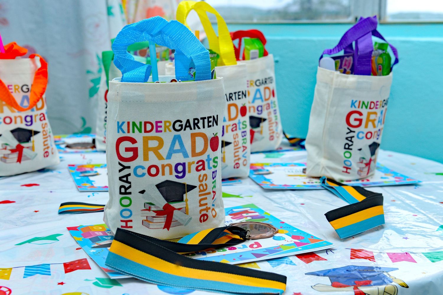 Colorful kindergarten graduation supplies with decorated bags and craft materials on a blue table.