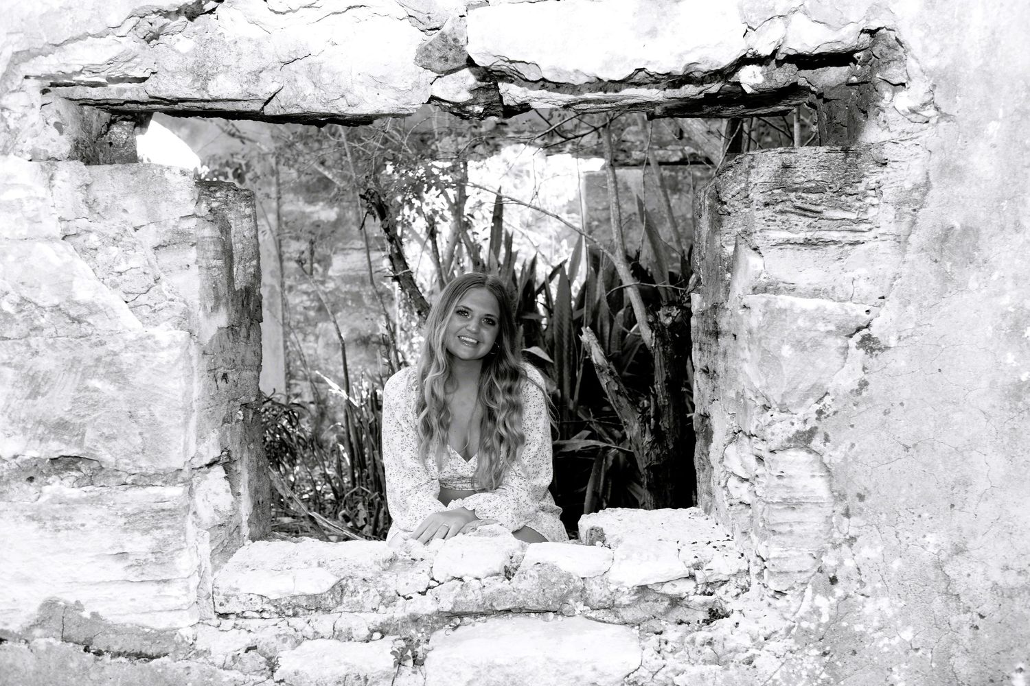 Black and white photograph showing a figure framed within a rustic stone window opening.