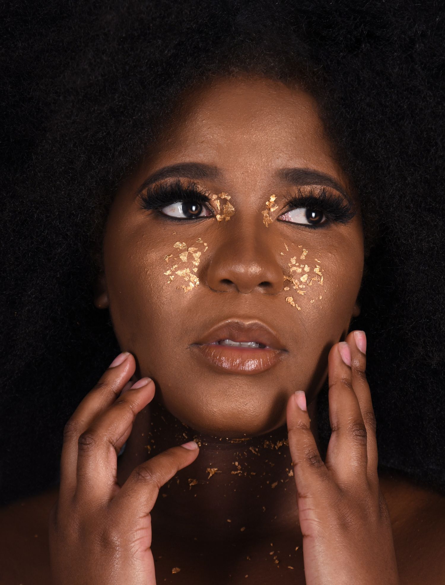 A beauty portrait featuring gold flecks on dark skin against a black background.