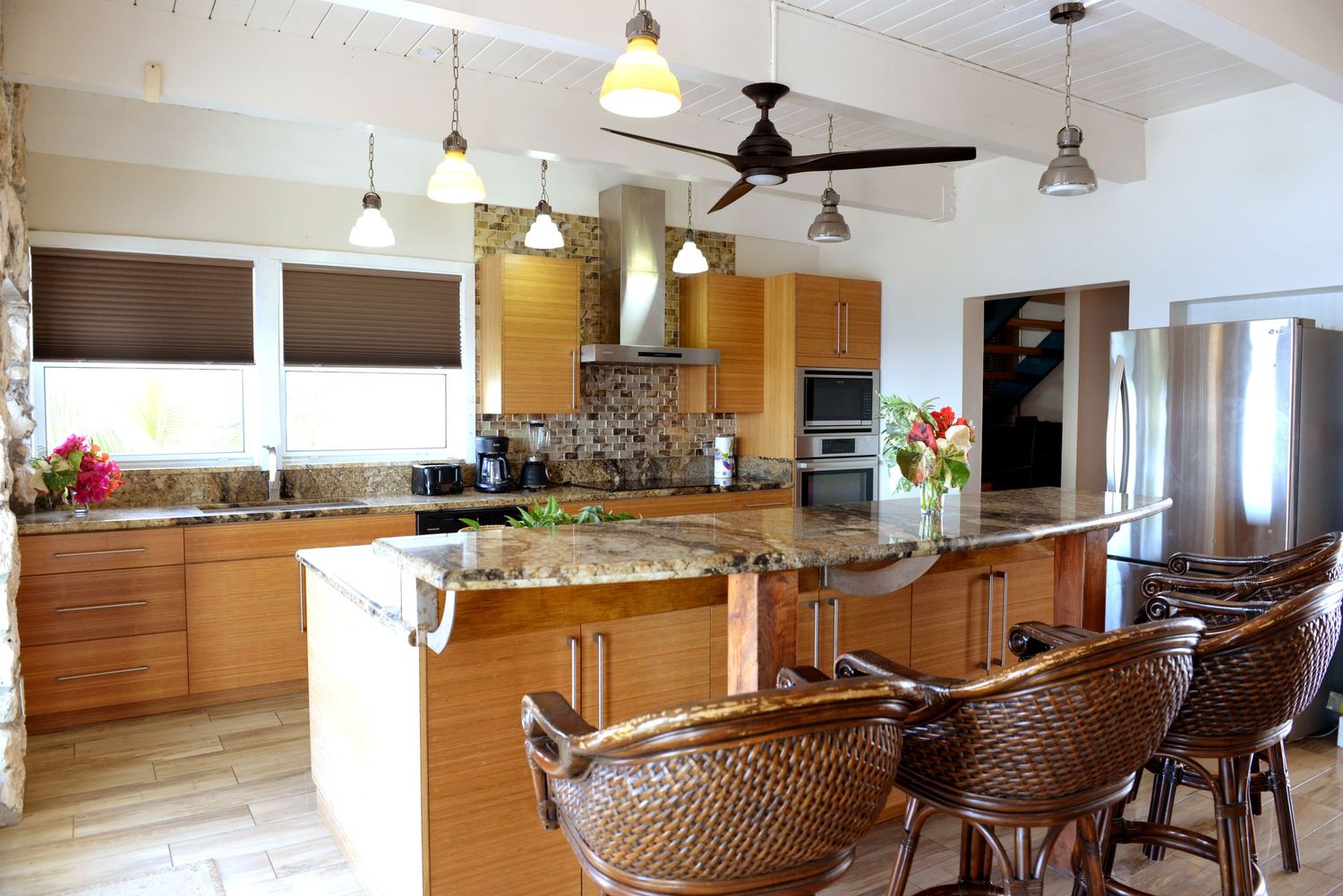 Modern tropical kitchen with wooden cabinets, granite countertops and woven rattan bar stools.
