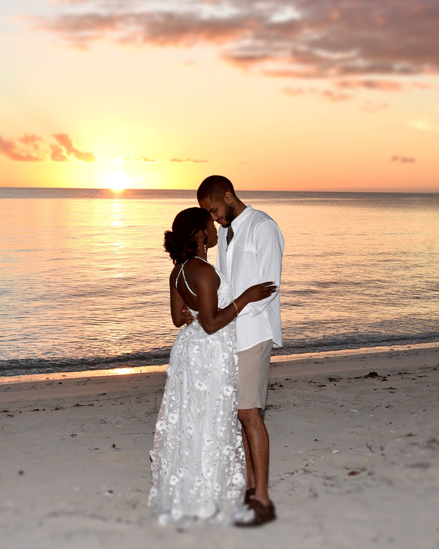Romantic beach wedding photo at sunset with ocean backdrop.