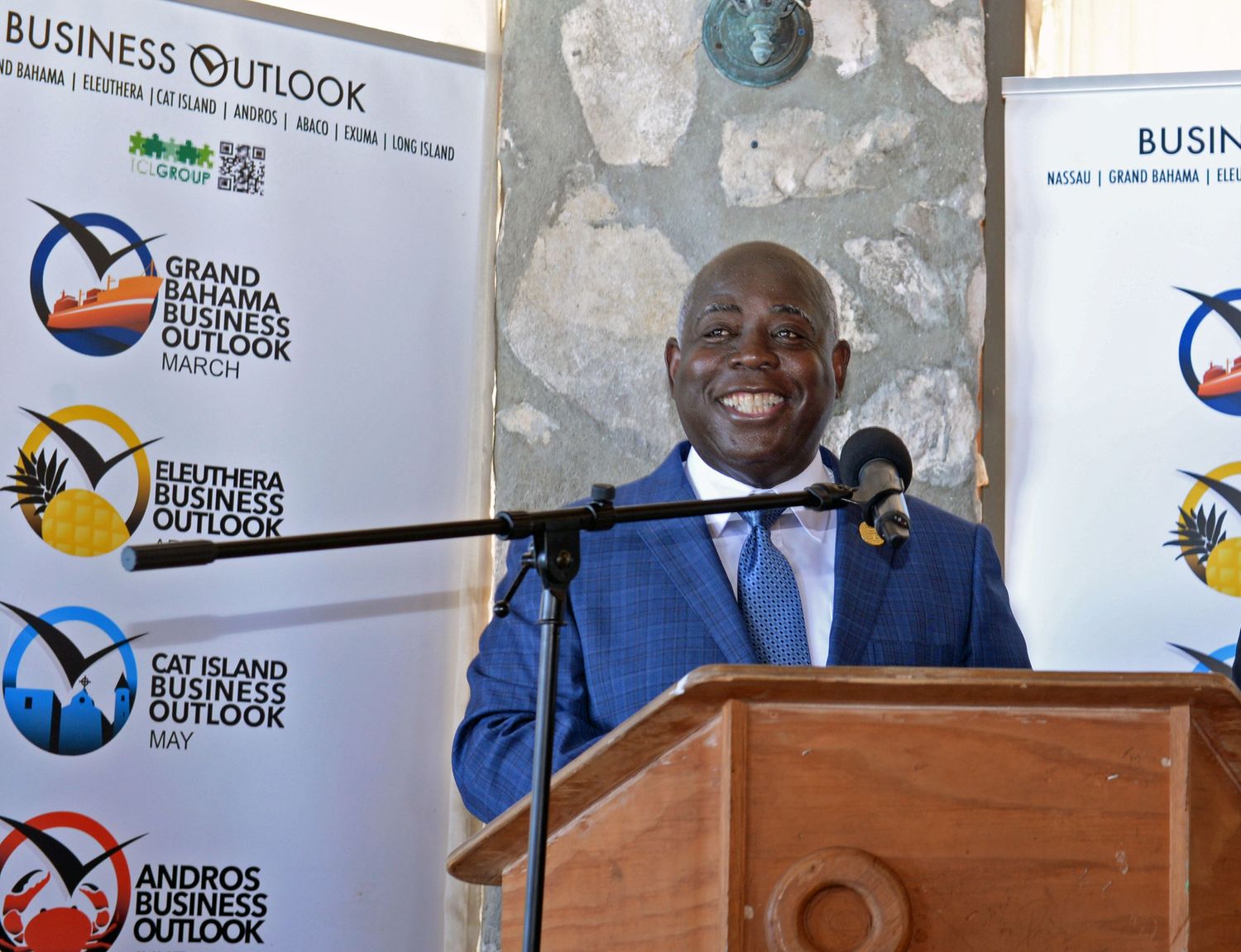 Prime Minister at a business podium with organizational logos displayed on banners behind.