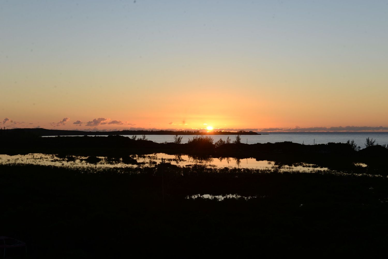 Dramatic sunset silhouette over a coastal landscape with water reflections.
