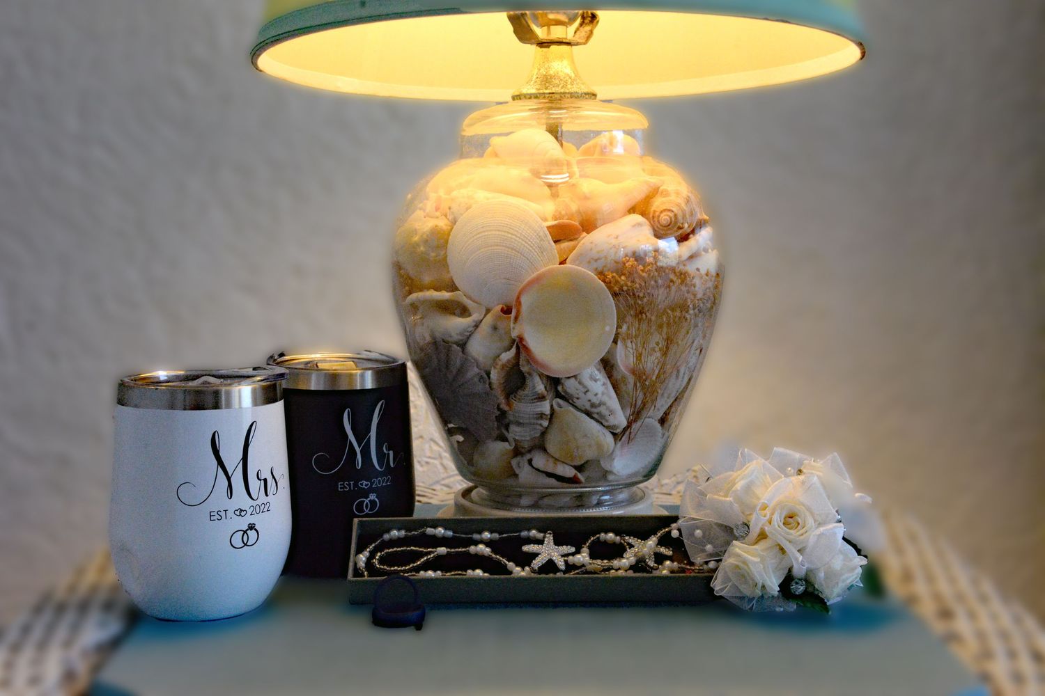 Decorative table lamp with seashell base and cream shade alongside matching his and hers coffee mugs