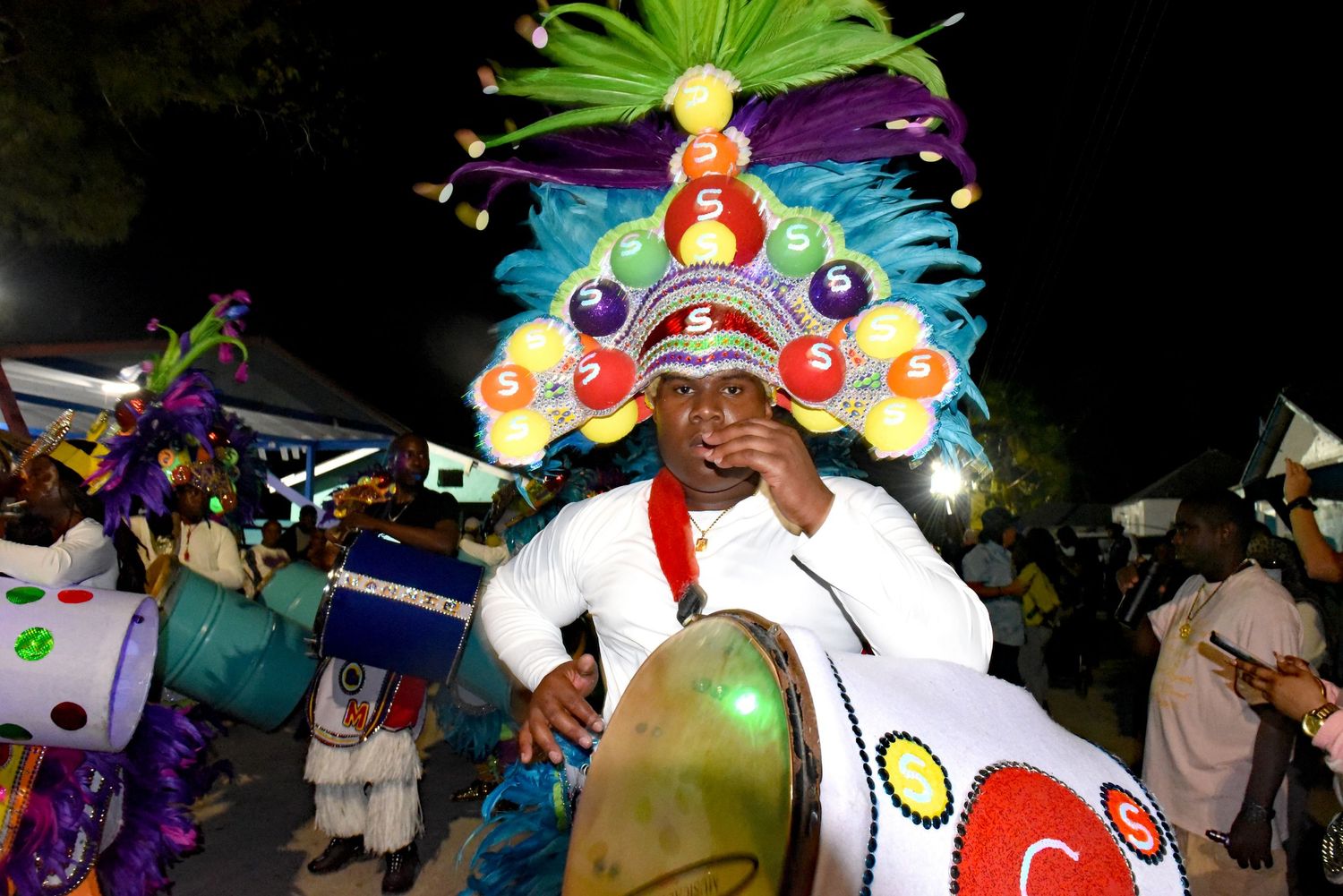 Festive Junkanoo performer wearing elaborate colorful headdress during nighttime celebration.