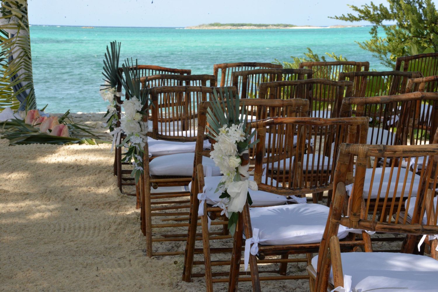 Wooden chairs decorated with white flowers set up for a beach wedding ceremony.