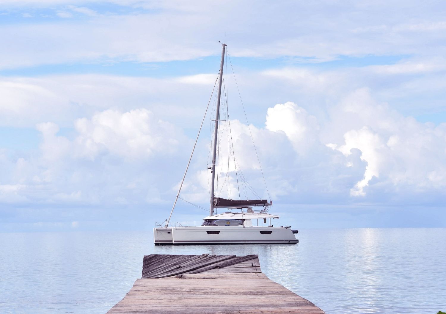 White catamaran yacht docked at wooden pier on calm tropical waters under blue sky.