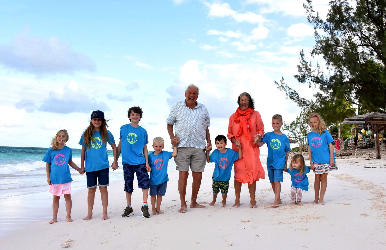 Group walking together on a tropical beach wearing coordinated blue and orange outfits.