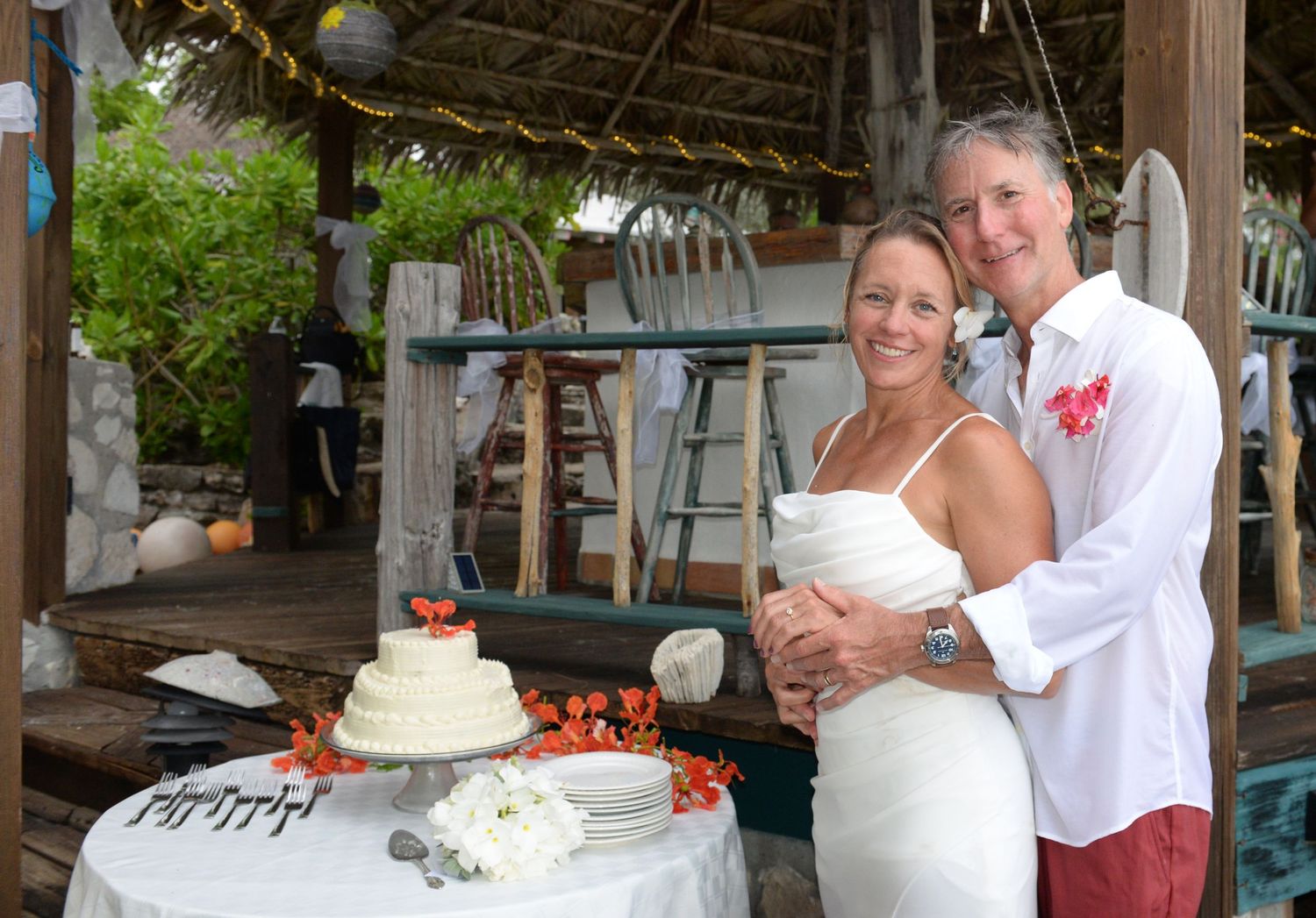 Beach wedding reception setup with cake and decorations under a thatched roof.