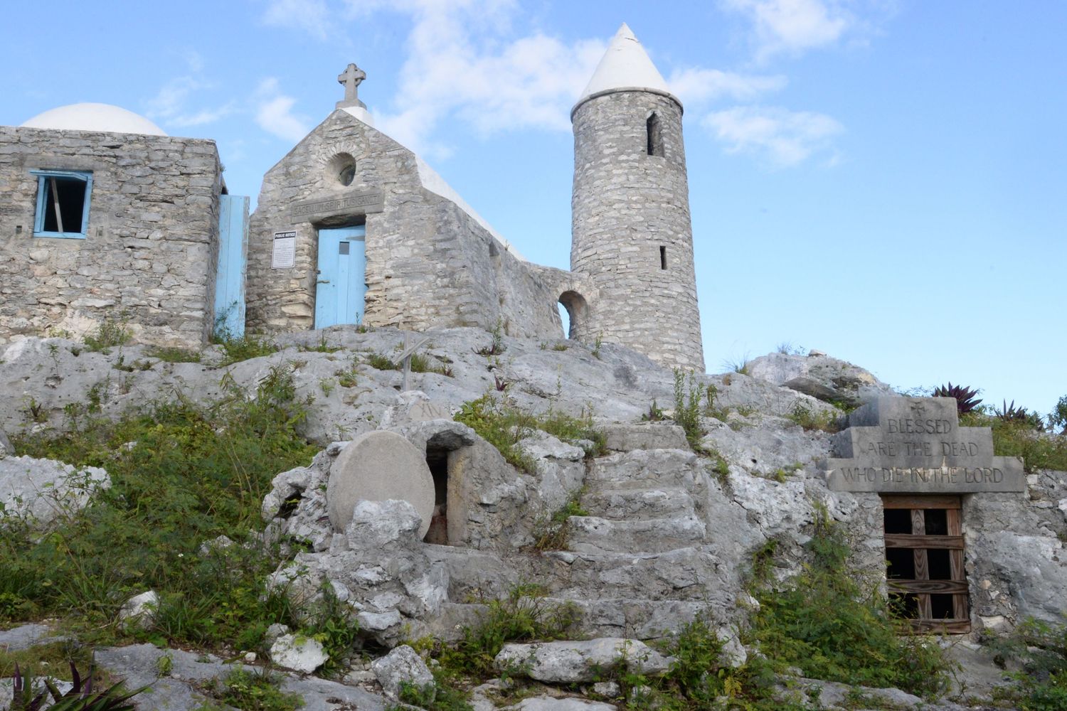 Ancient stone ruins of a medieval church or monastery with crumbling walls and arched windows stand against a blue sky.