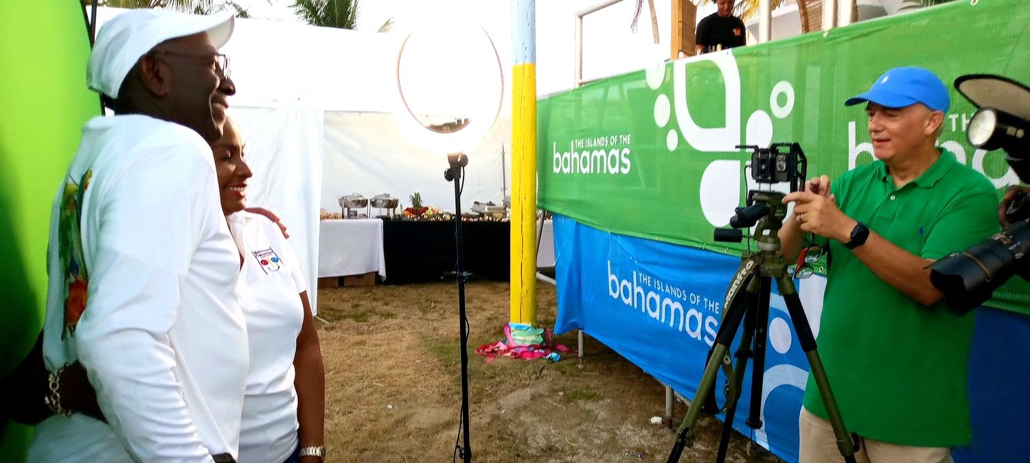 Person in white hoodie interacts with volunteer at green and blue outdoor event booth.
