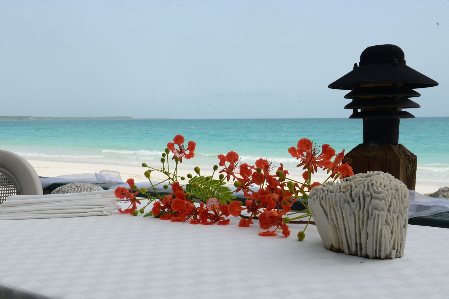 Orange flowers and a black lantern decorate a table setting against a turquoise ocean backdrop.