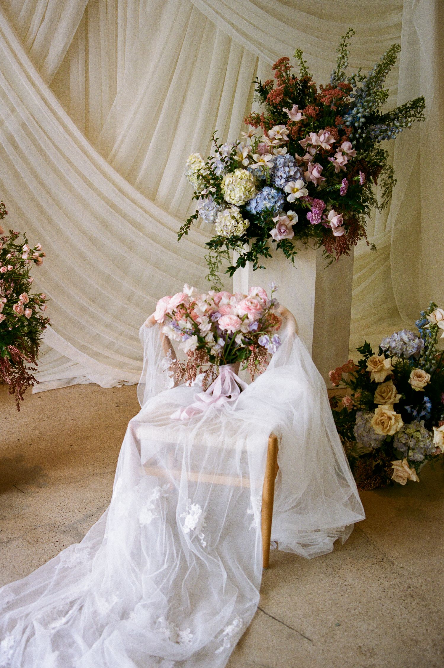 Elegant wedding setup with a floral bouquet on a draped chair surrounded by colorful arrangements.