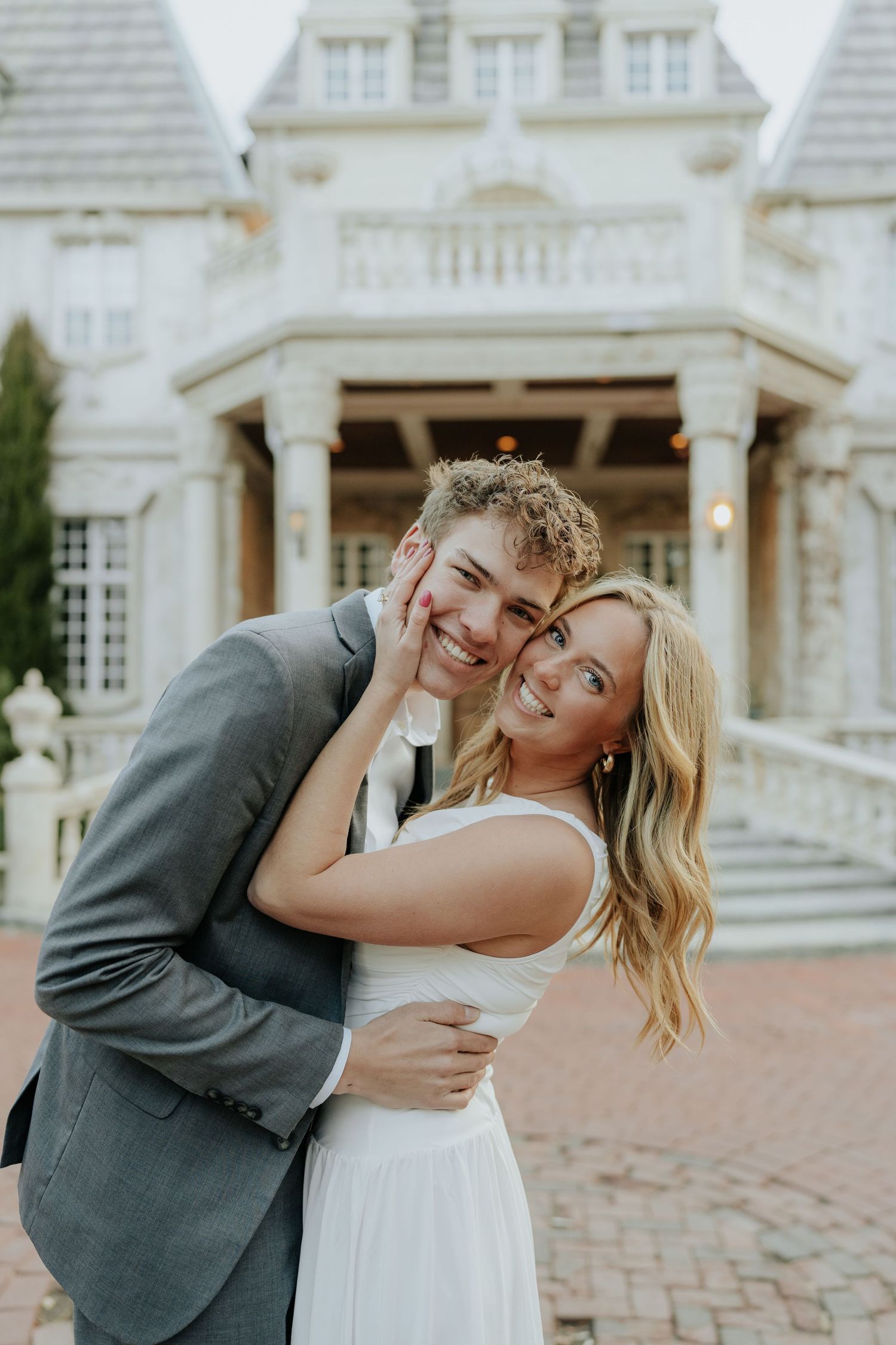 Happy couple embracing and smiling in front of an elegant white manor house at dusk at La Caille Restaurant in Utah.