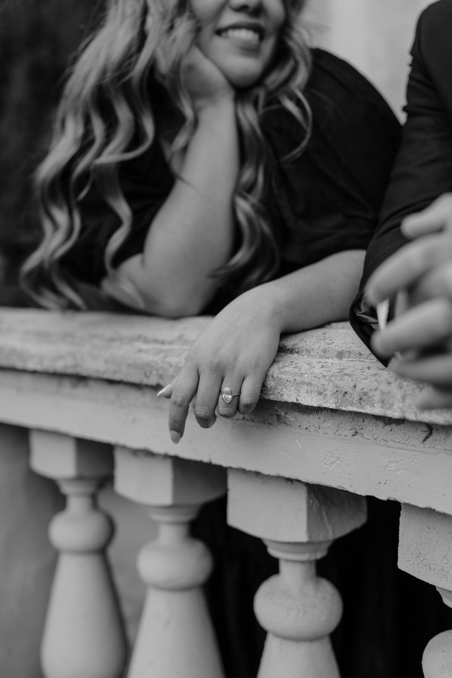 Black and white close-up of smiling bride leaning on balustrade showing engagement ring at La Caille Restaurant in Utah.