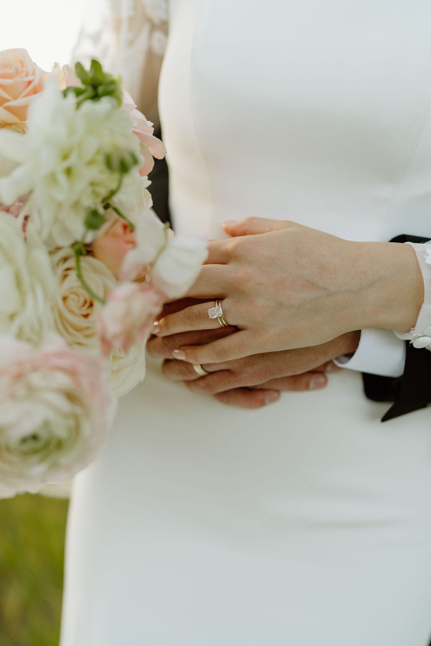 Close-up of bride's diamond engagement ring and wedding bouquet of blush and white roses.