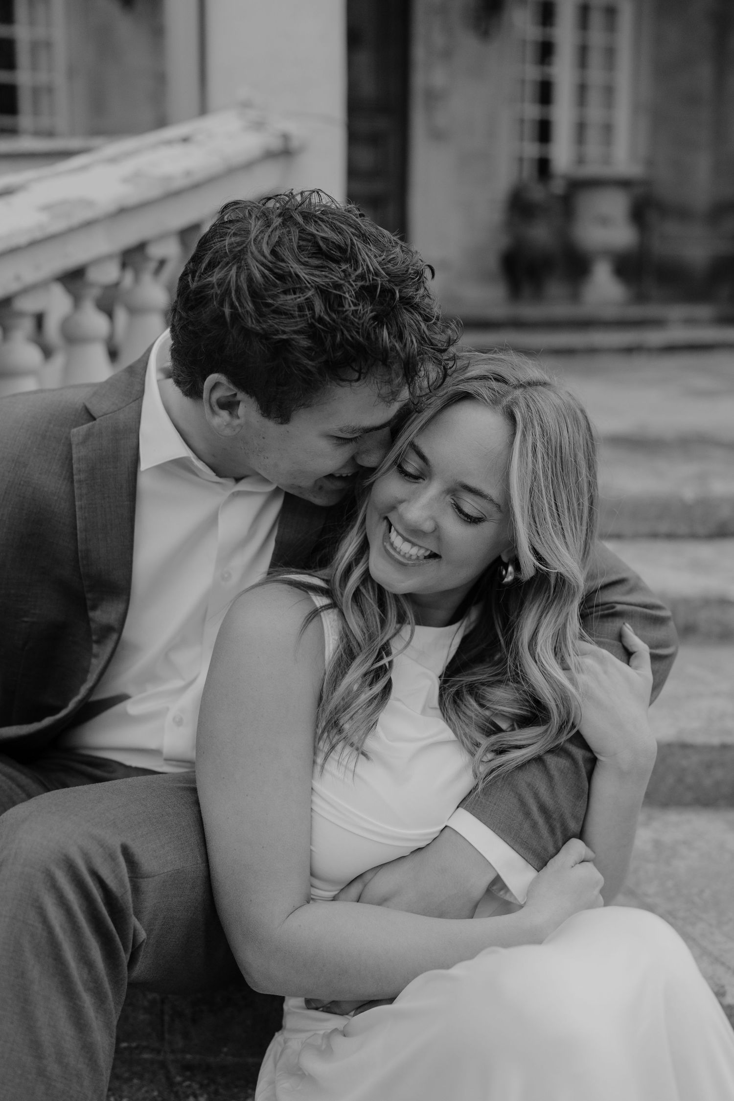Black and white photo of couple sharing a tender moment, man kissing womans temple as she laughs at La Caille Restaurant in Utah.