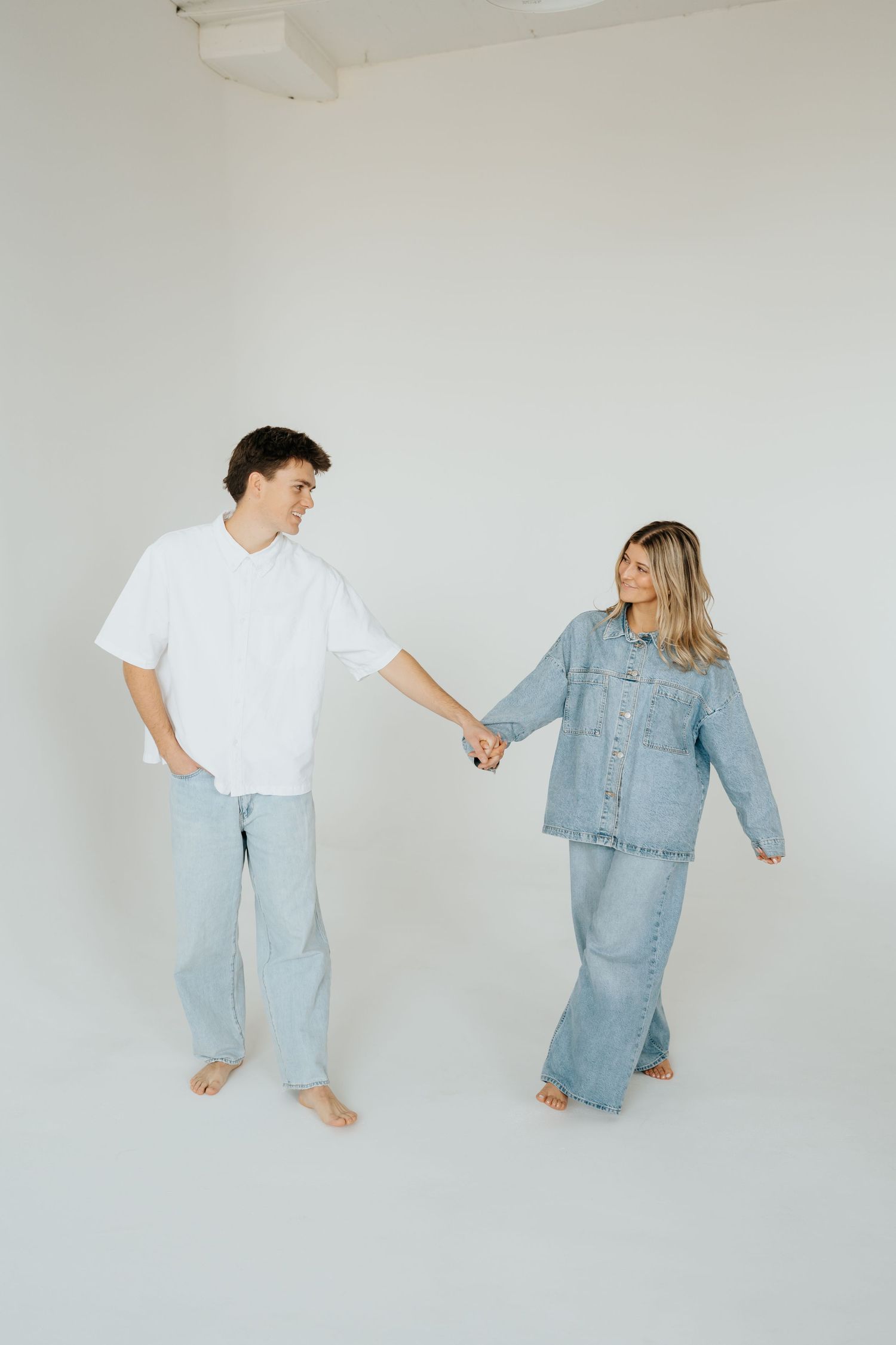 Couple holding hands in at Studio Elevn in Salt Lake City, Utah, both wearing denim outfits, smiling at each other.