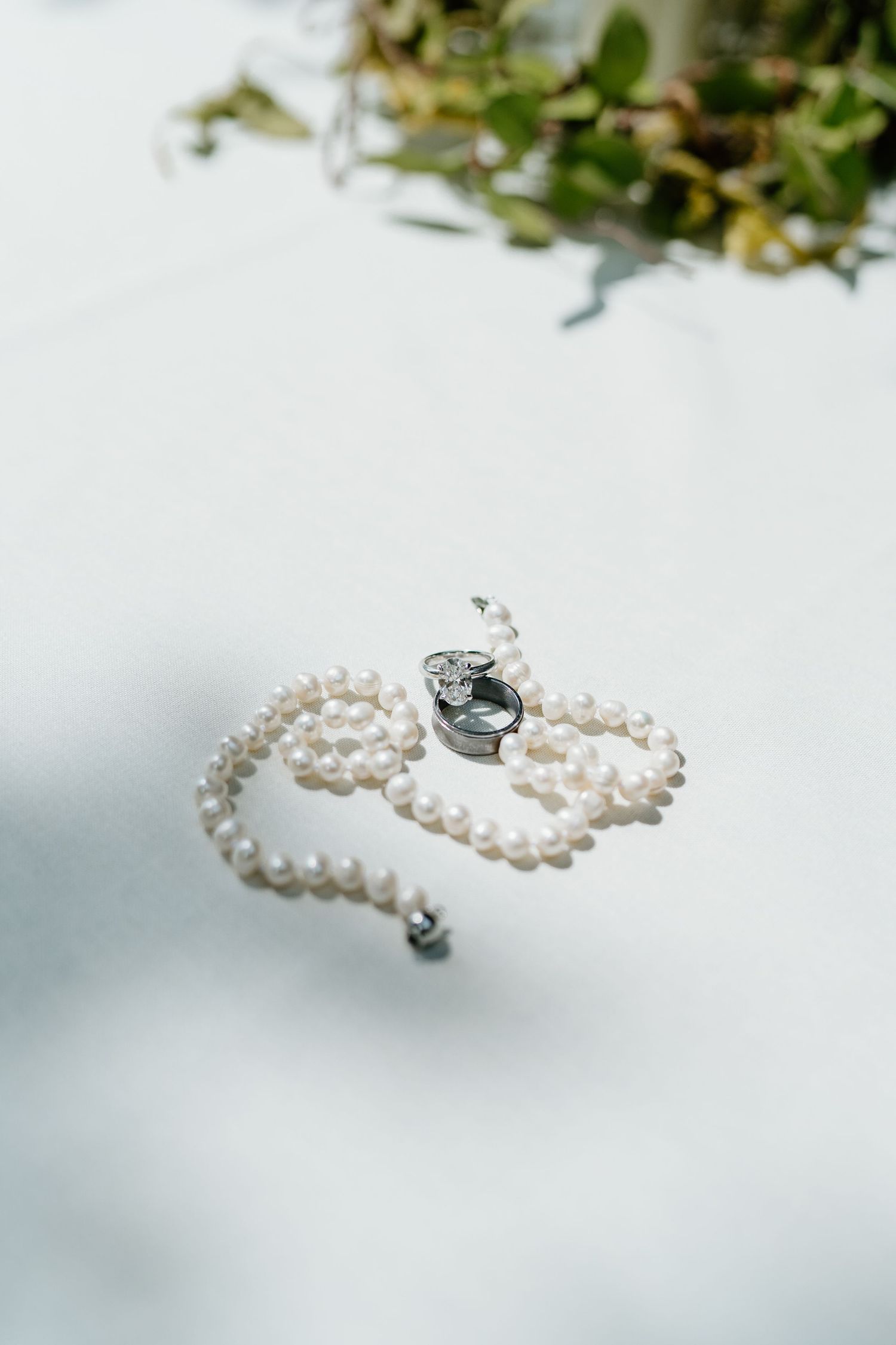 Pearl necklace with diamond clasp elegantly arranged on white surface with greenery.