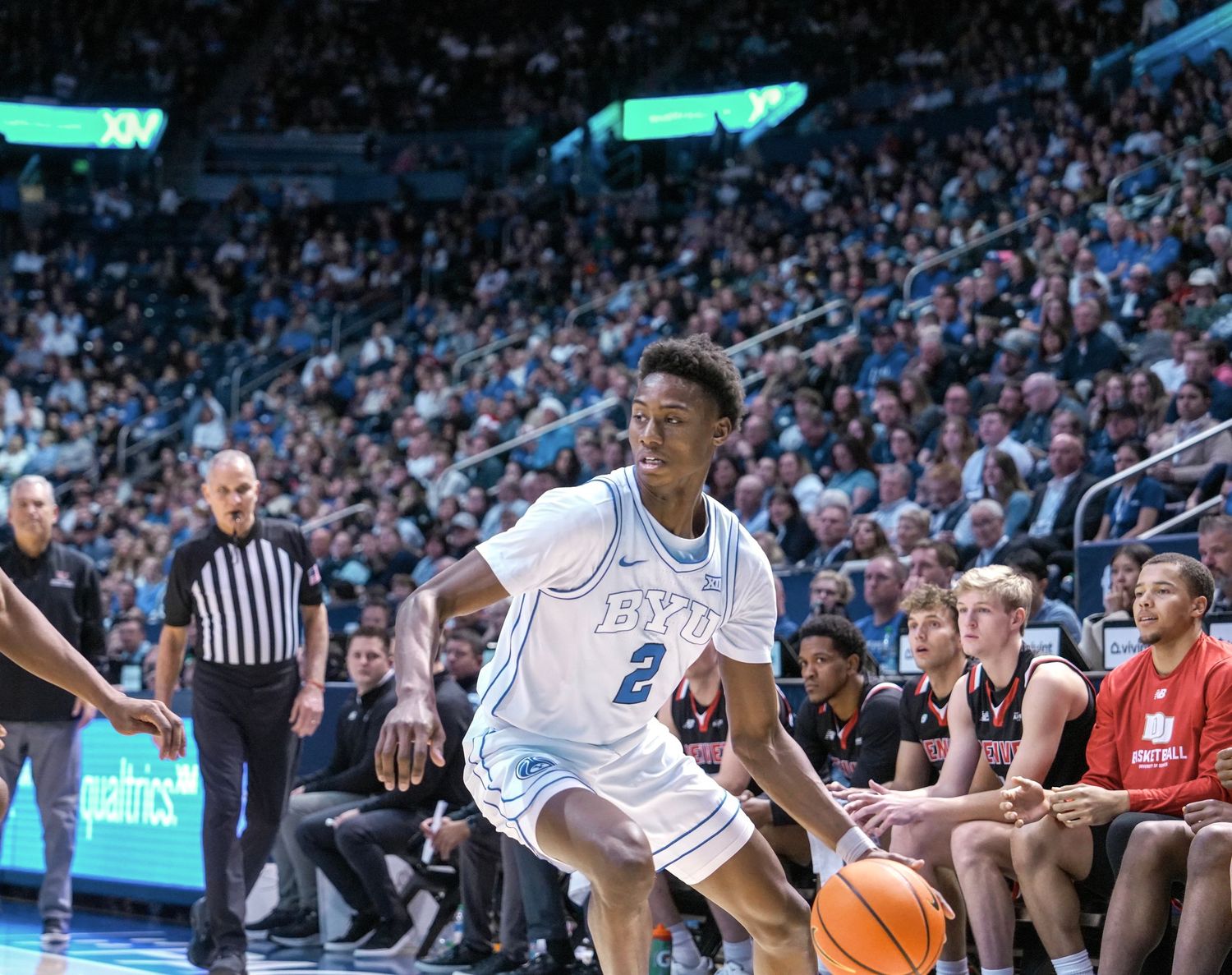 Basketball player wearing number 2 dribbles toward the basket during a college game in a packed arena.