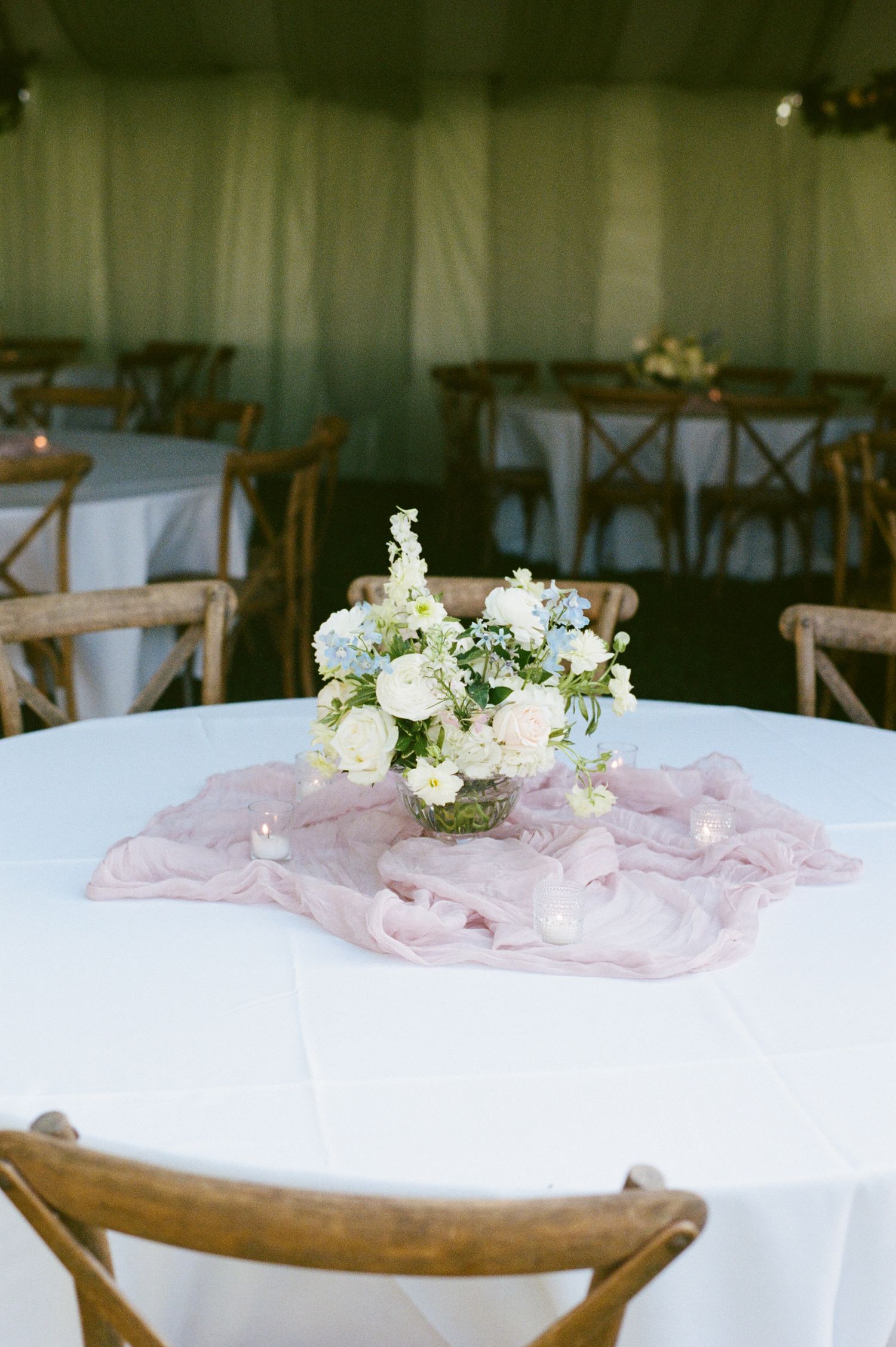 Elegant wedding reception table with white linen, pink chiffon runner, and blue and white floral centerpiece.