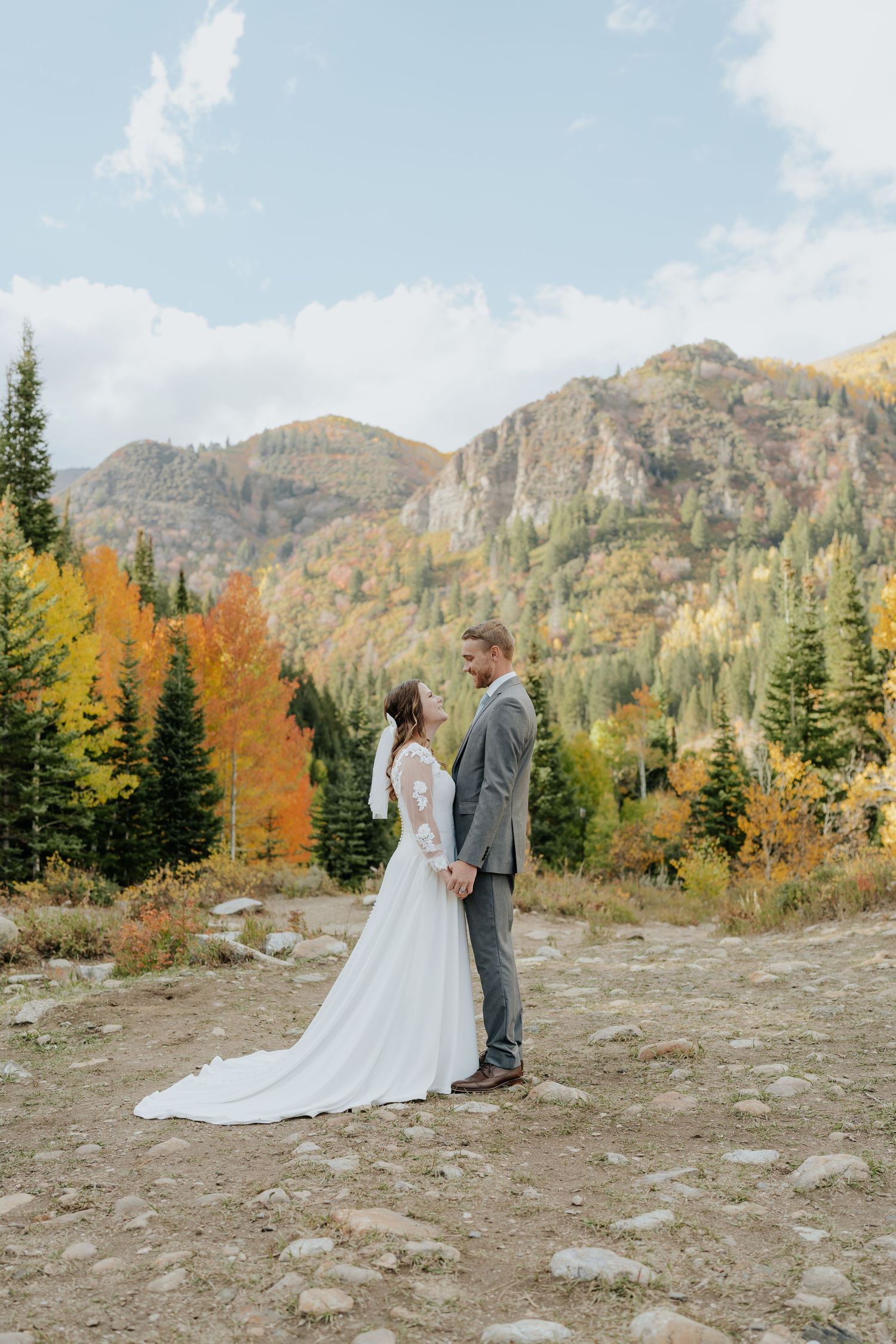 Bride and groom holding hands facing each other with stunning autumn mountain landscape behind them.