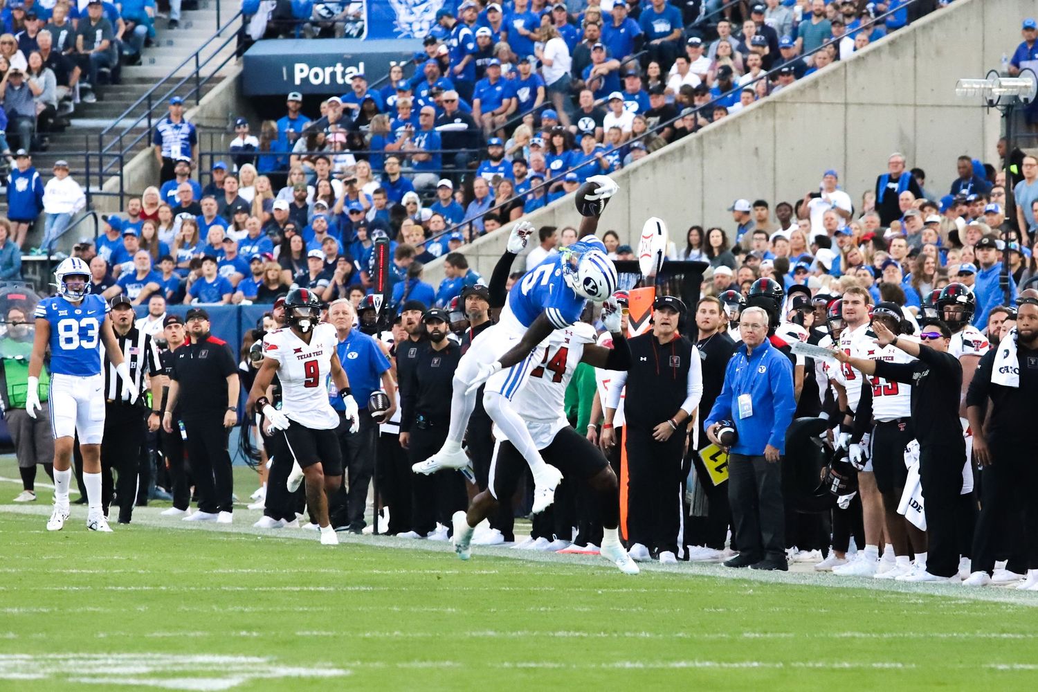 Football players leap near the sideline during an action-packed college football game in a packed stadium.