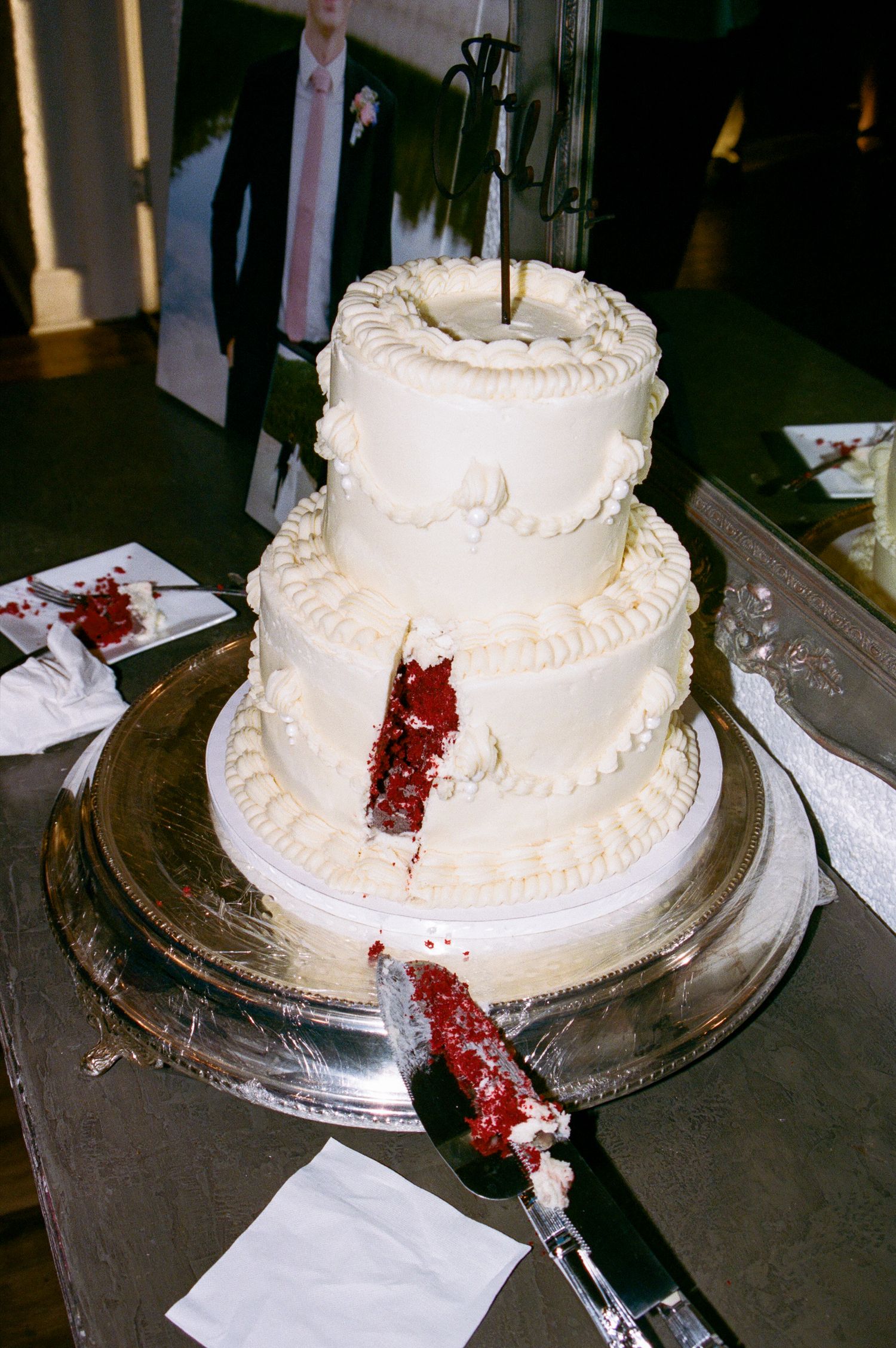 Two-tier white frosted red velvet wedding cake with a slice cut out on a silver stand.