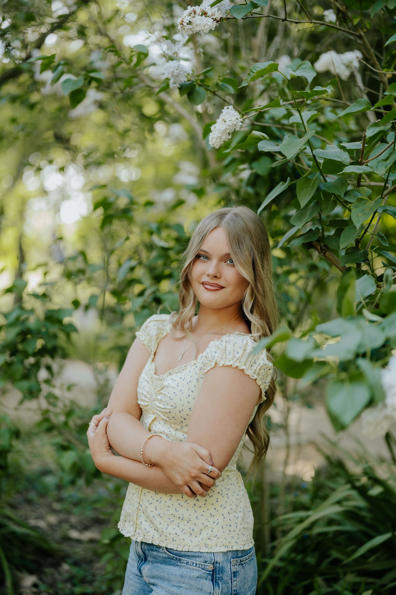 Smiling blonde teen girl in floral top posing among white flowering bushes in garden near Sacramento, California.