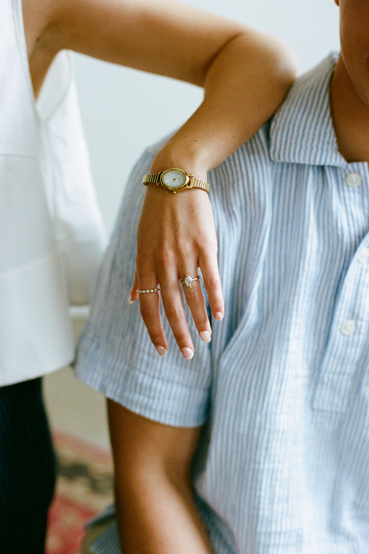 Close-up of a bride's hand wearing a diamond engagement ring and gold watch on a blue striped dress.