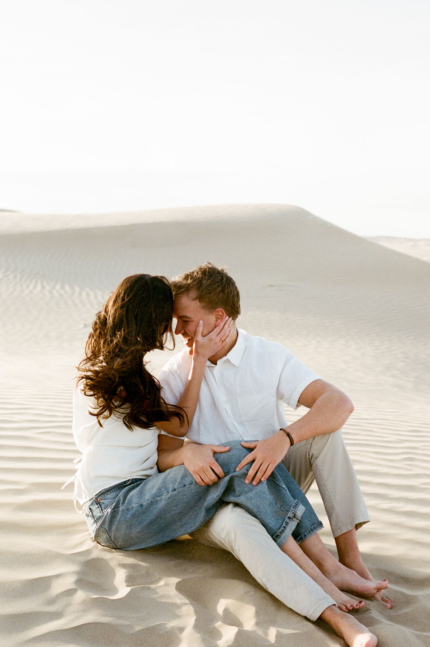 Couple sharing a kiss while sitting barefoot on desert sand dunes at sunset at Little Sahara Sand Dunes.