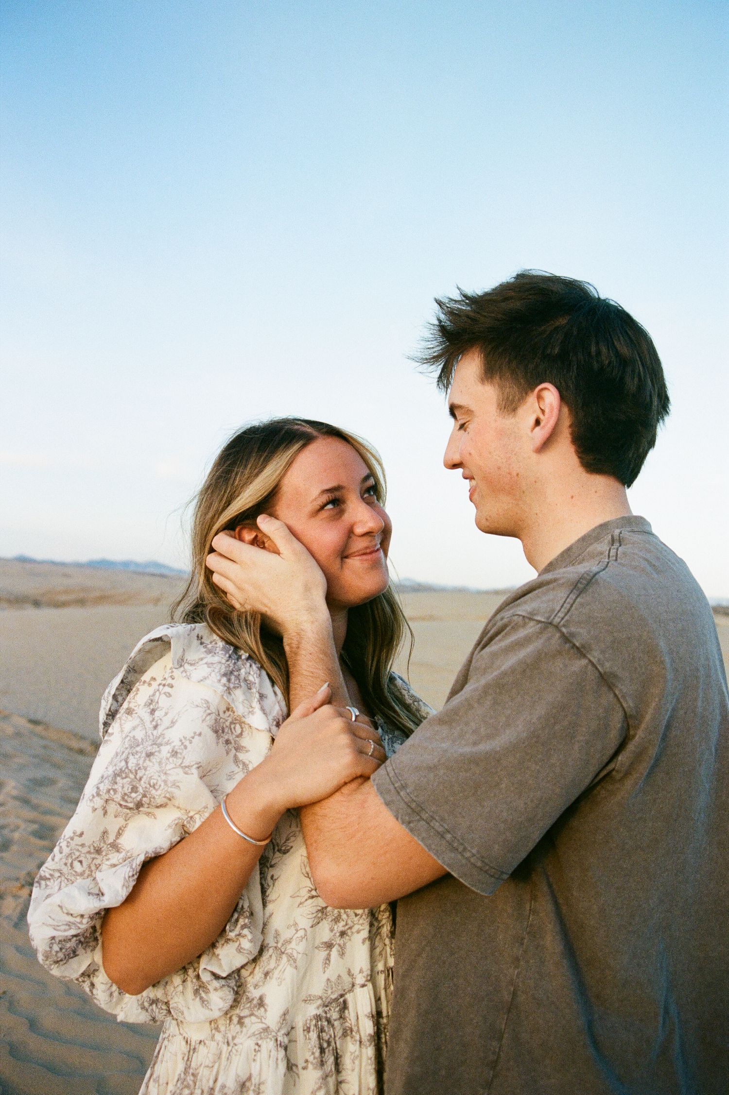 Couple embracing and smiling at each other on sandy desert dunes at golden hour.