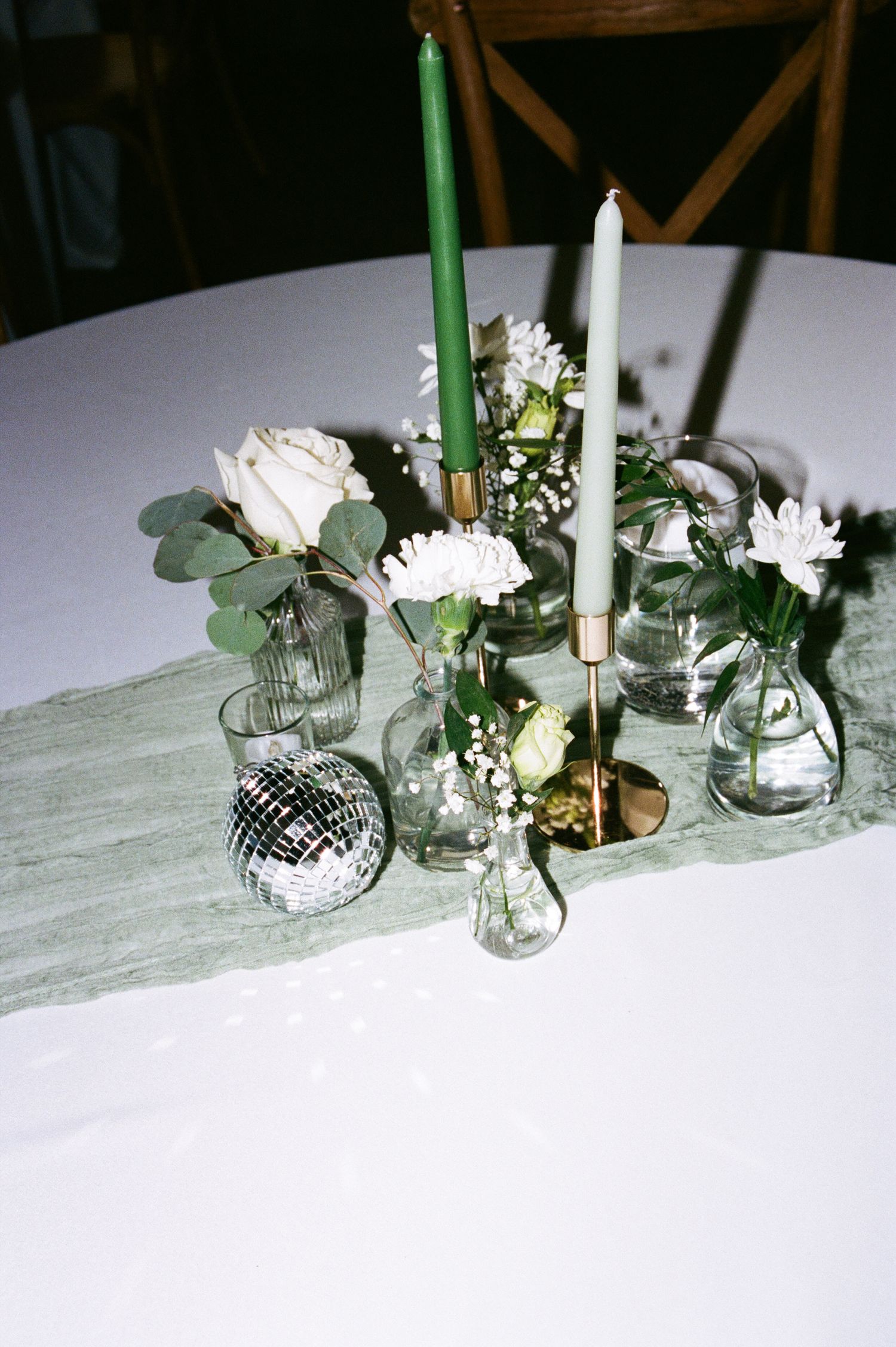 Elegant wedding table centerpiece with green candles, white roses, and a mini disco ball.