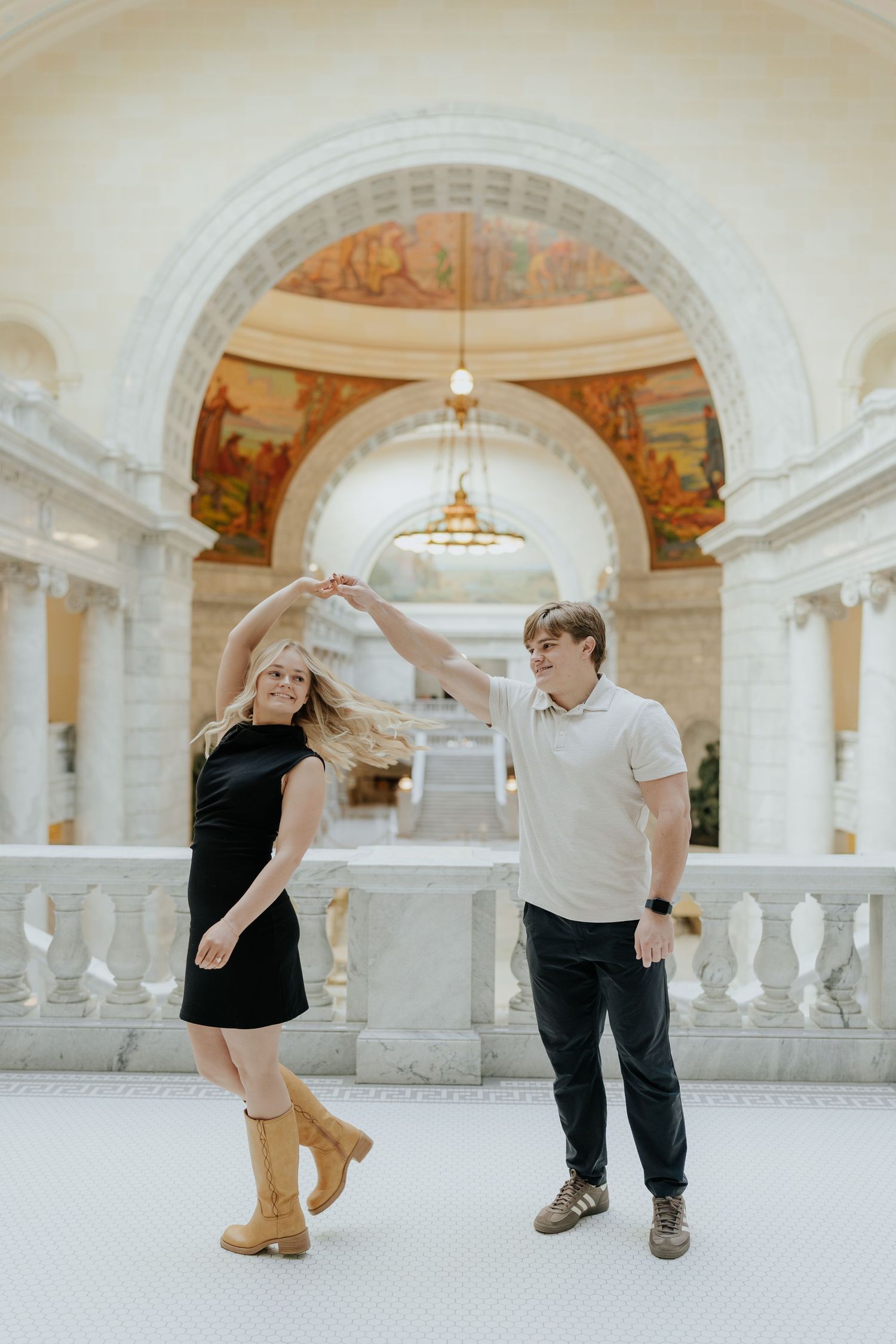 Couple dancing elegantly inside a grand marble building with ornate murals and arched ceilings at the Utah State Capitol Building.
