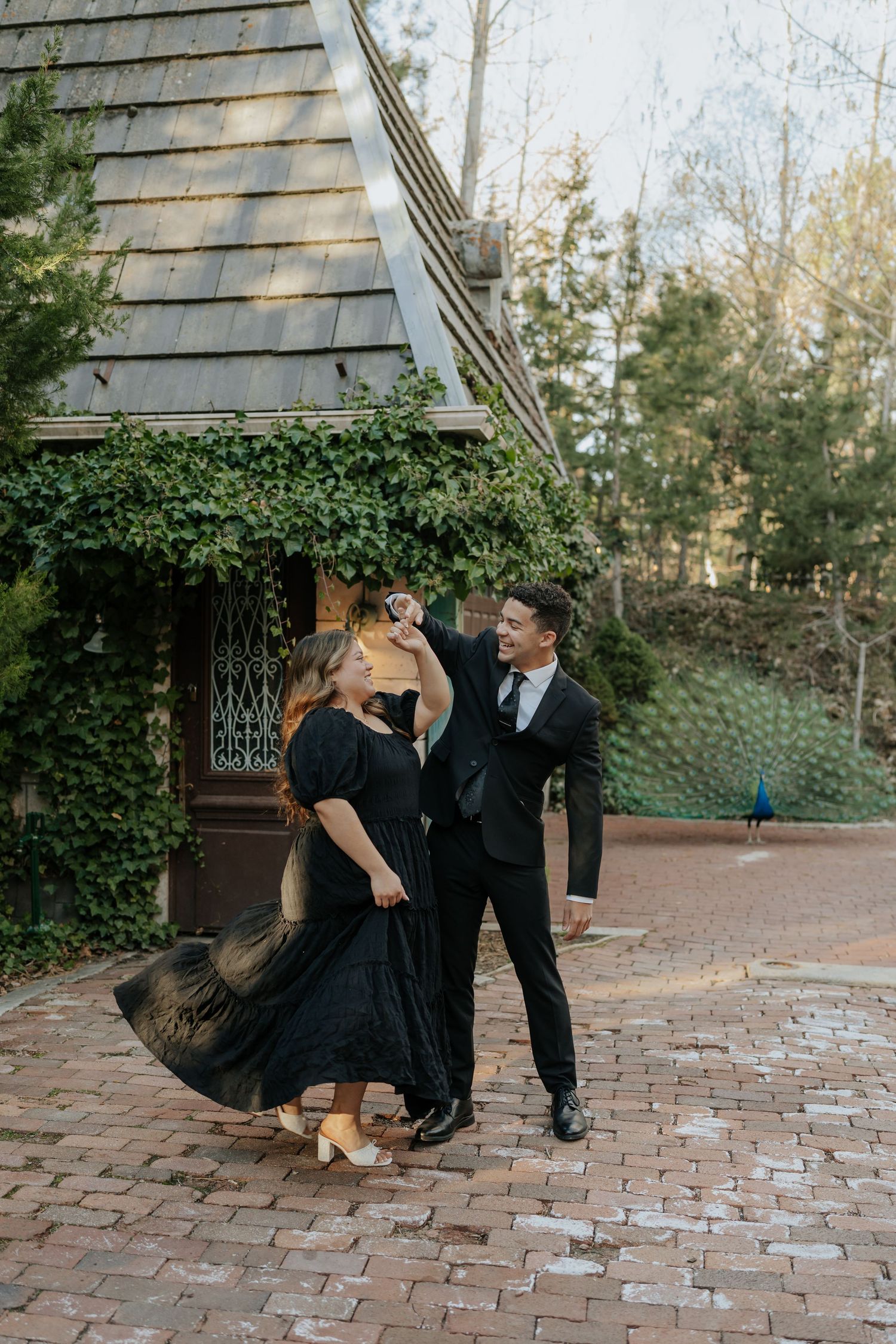 Couple dancing outdoors near ivy-covered cottage in elegant black formal attire at La Caille Restaurant in Utah.