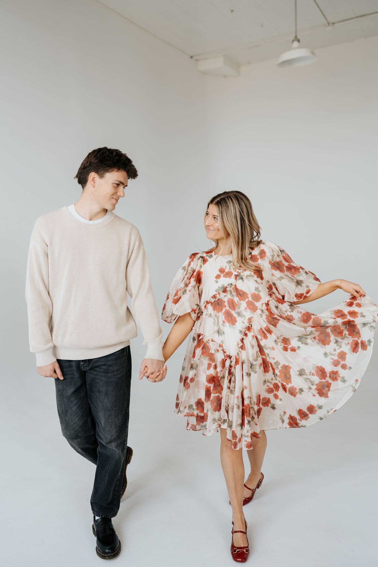 Couple walking hand in hand at Studio Elevn in Salt Lake City, Utah, woman in floral dress, man in cream sweater.