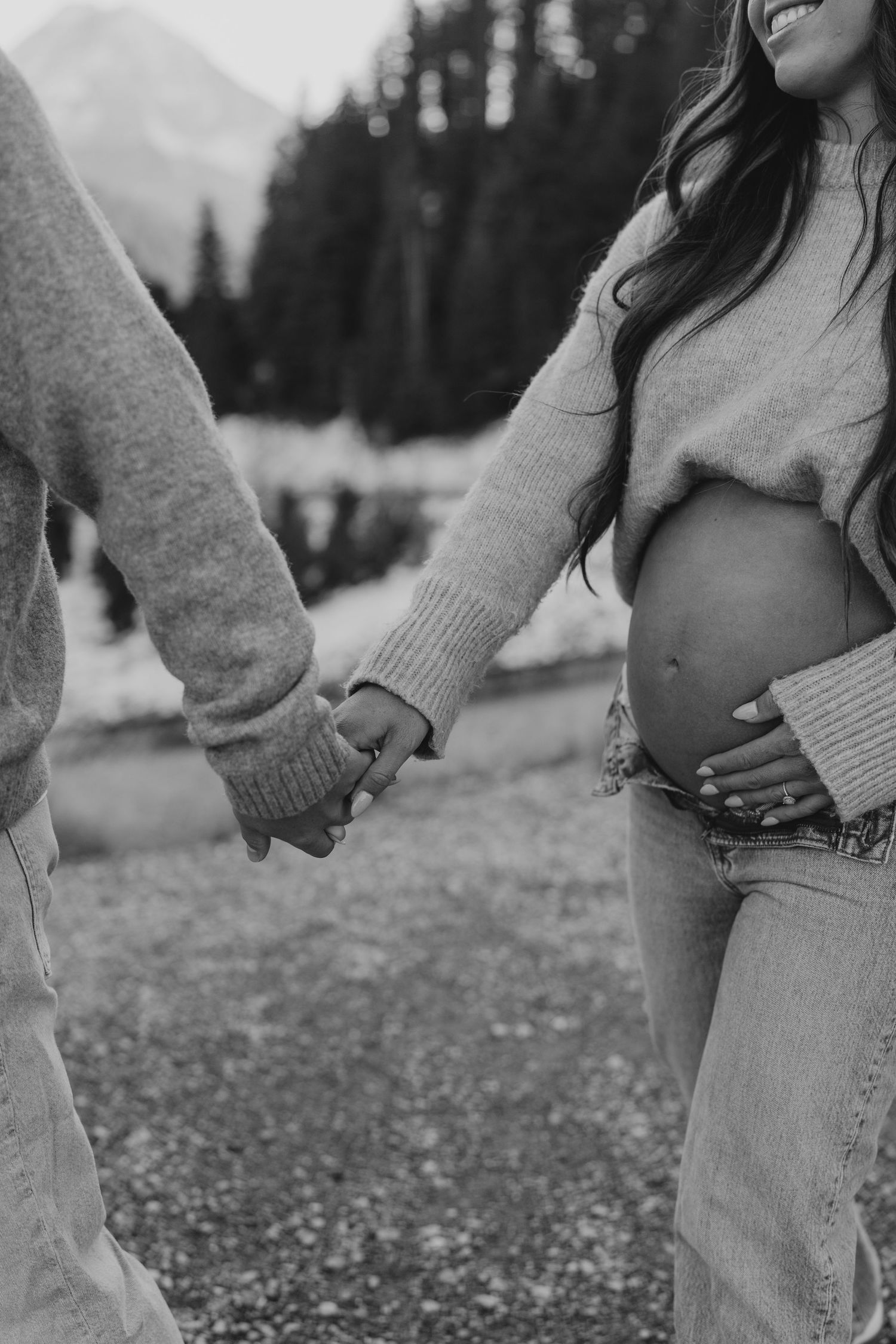Black and white image of pregnant couple holding hands, woman cradling bump in cozy sweater.