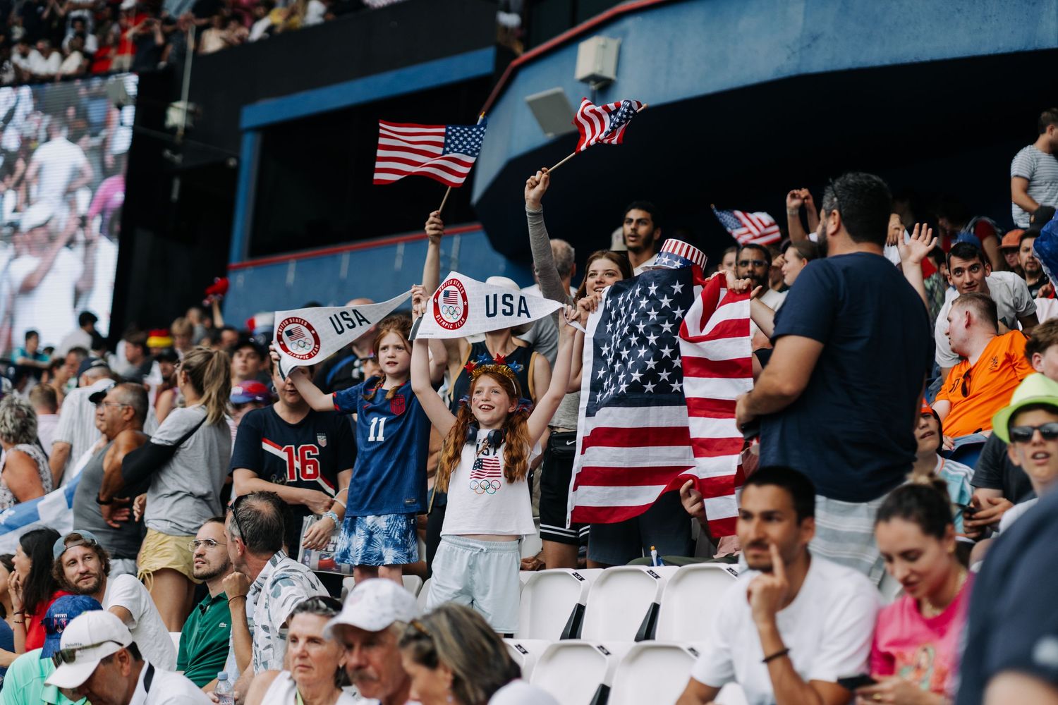 Enthusiastic USA fans wave American flags in the stands at the Paris 2024 Olympic Games.