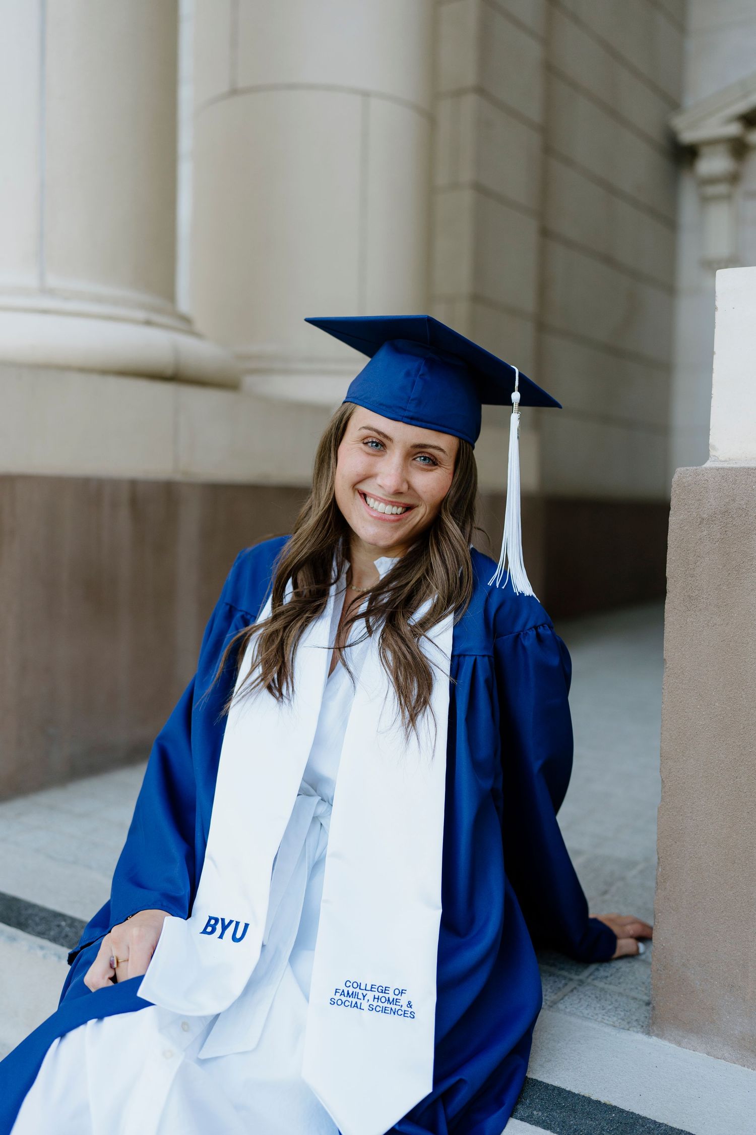 BYU graduate smiling in blue cap and gown with College of Family Home and Social Sciences stole.