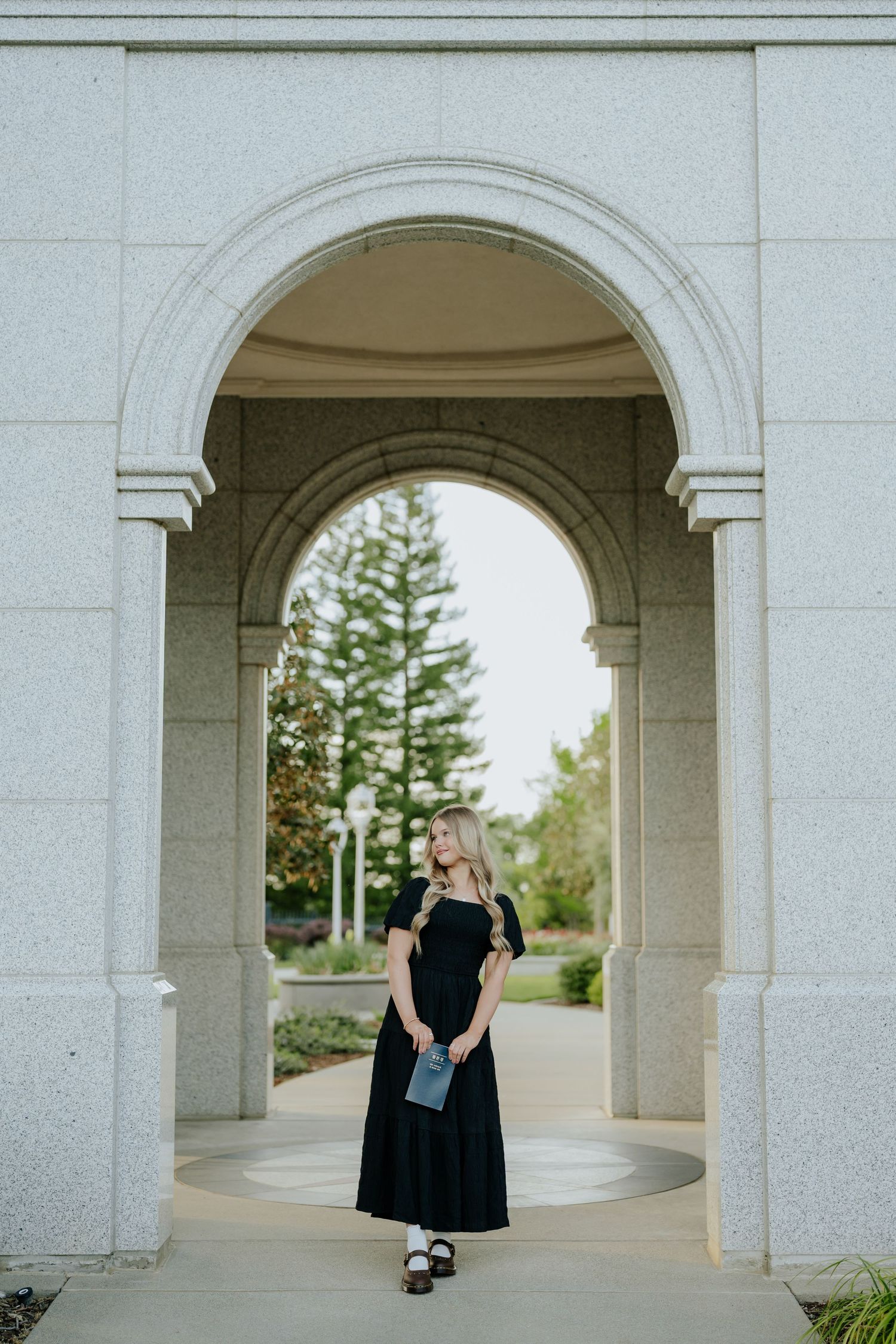 Blonde woman in black dress standing under stone archway at Sacramento LDS temple