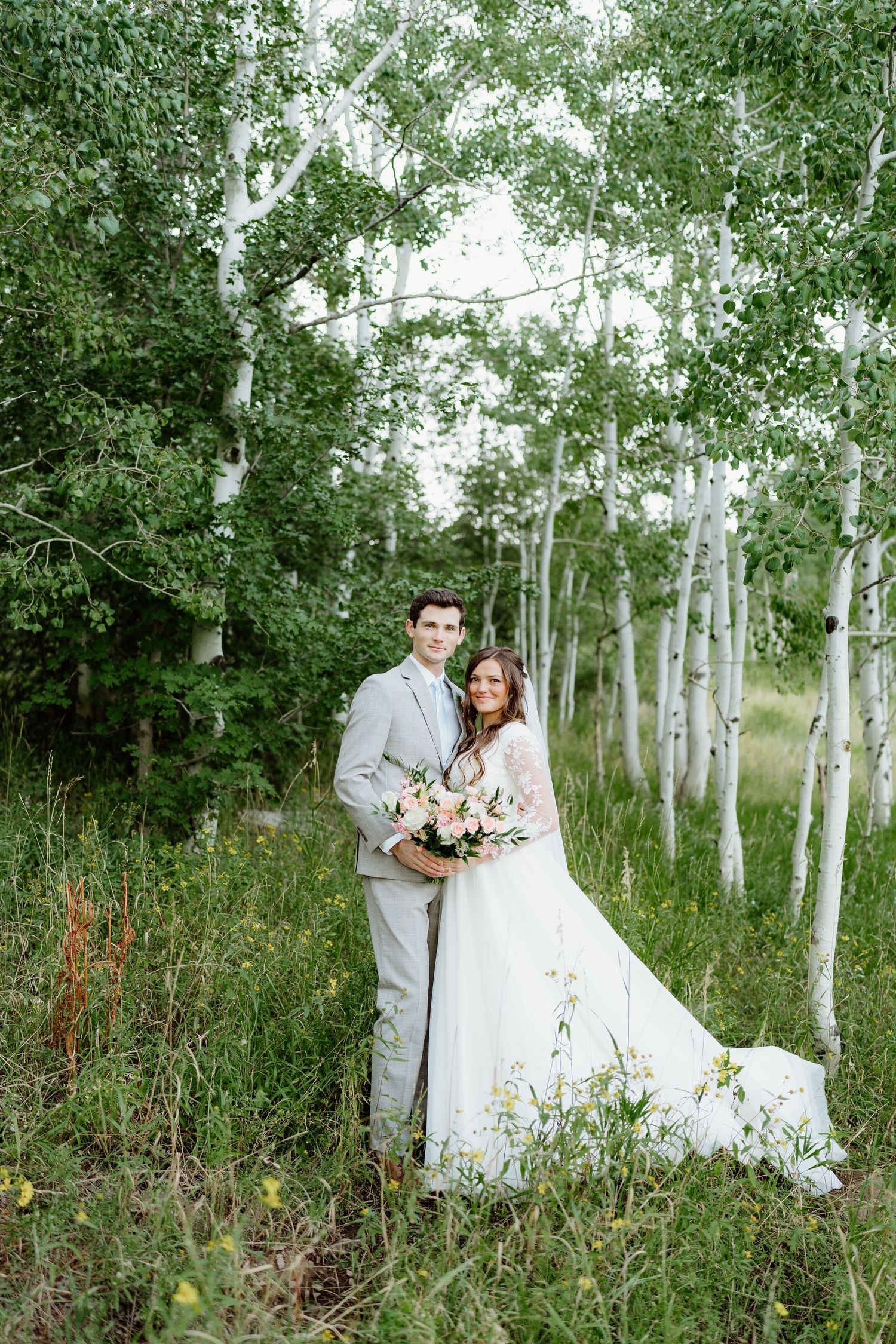 Bride and groom posing among white birch trees in a lush green forest setting.