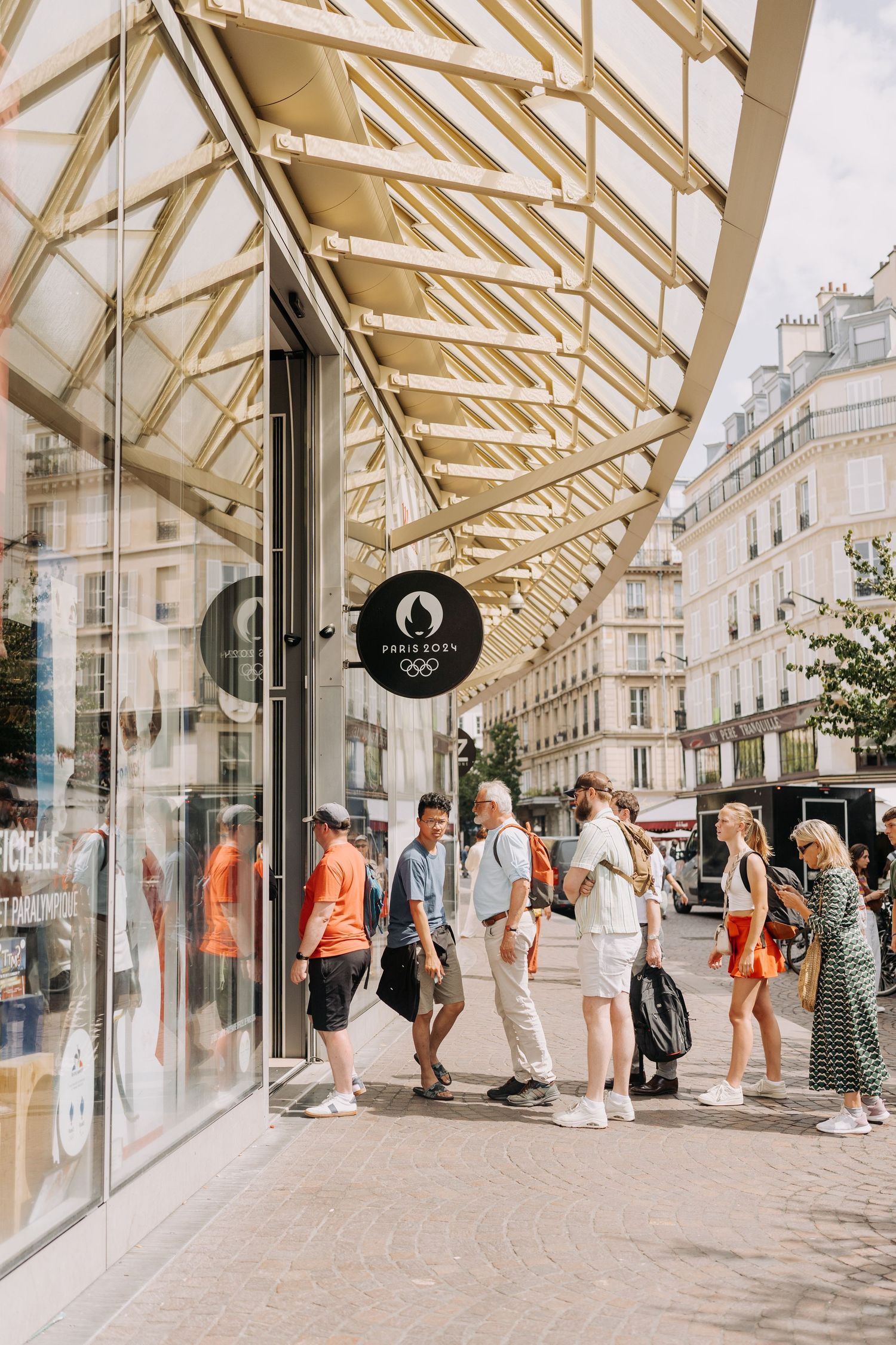 People queuing outside official Paris 2024 Olympics store on a sunny urban street in Paris.