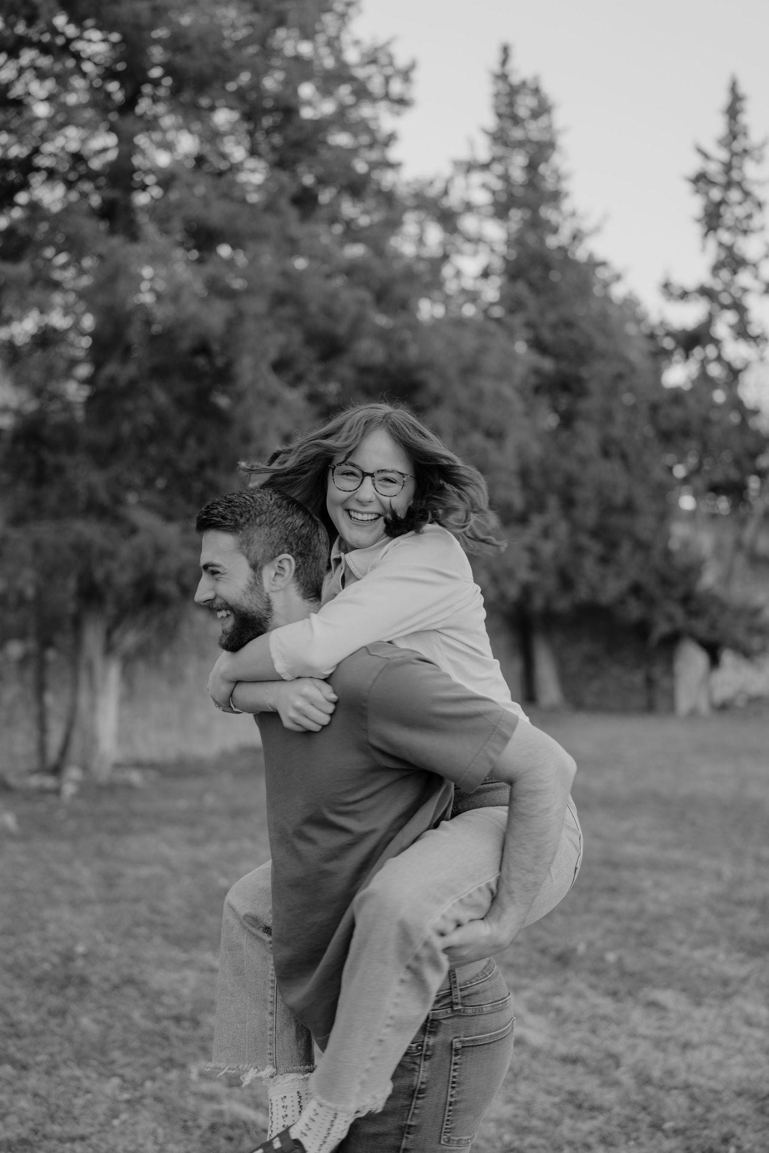 Black and white photo of laughing woman enjoying a piggyback ride from her partner in a park.