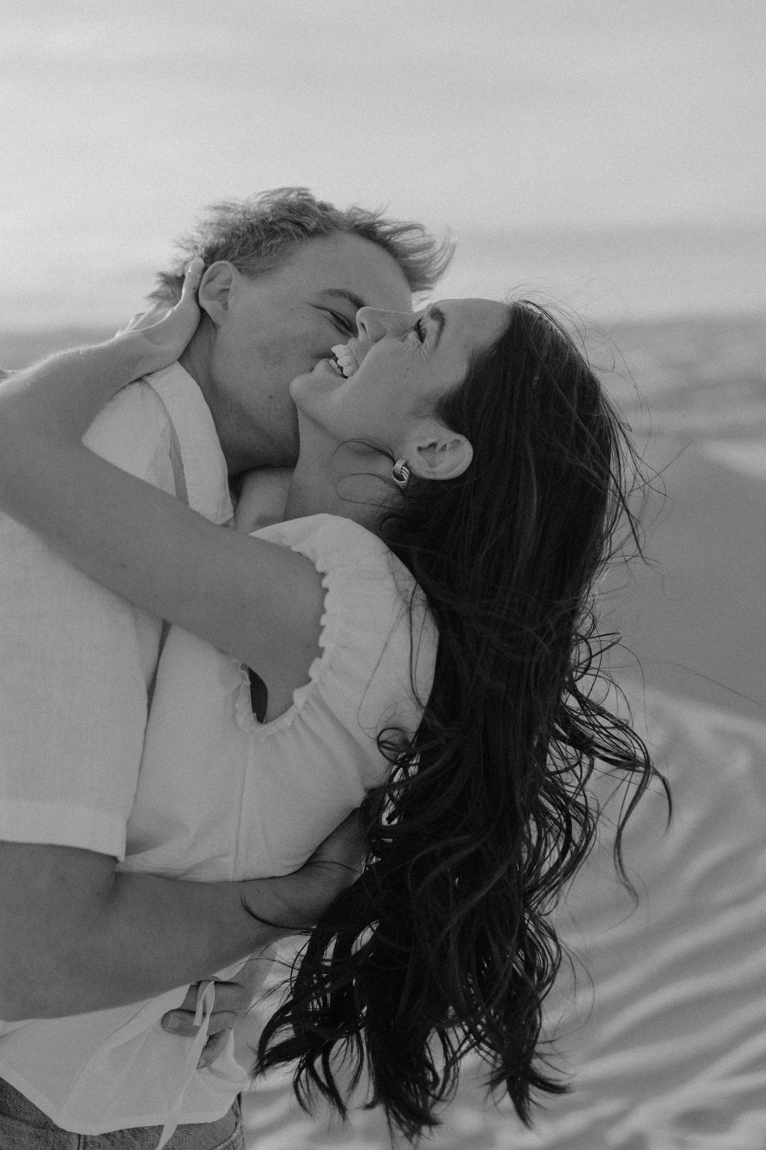 Black and white photo of couple embracing and kissing on windy sand dunes at Little Sahara Sand Dunes.