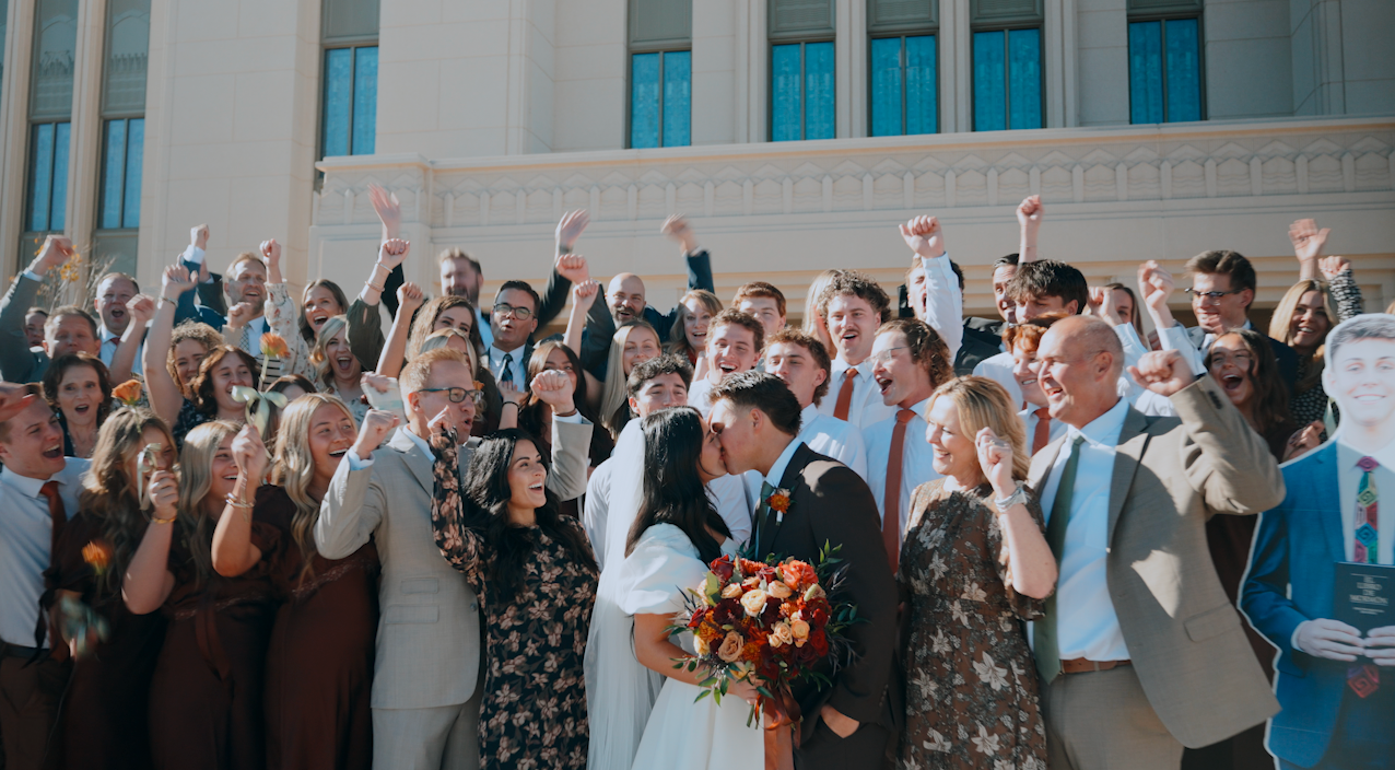 Bride and groom kissing surrounded by cheering wedding guests on Saratoga Springs temple steps.