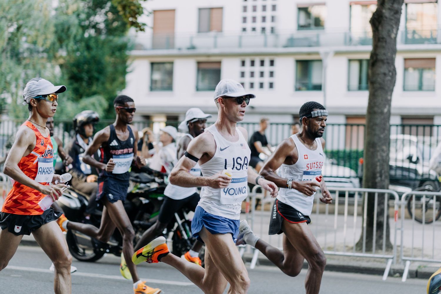 Male marathon runners compete on a city street during the Paris 2024 Olympic Games.