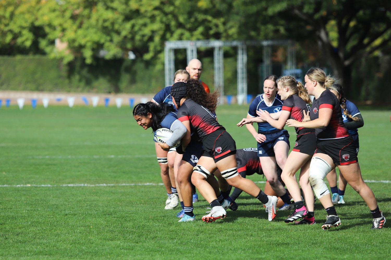 Female rugby players engage in a tackle during an outdoor match on a green grass field.